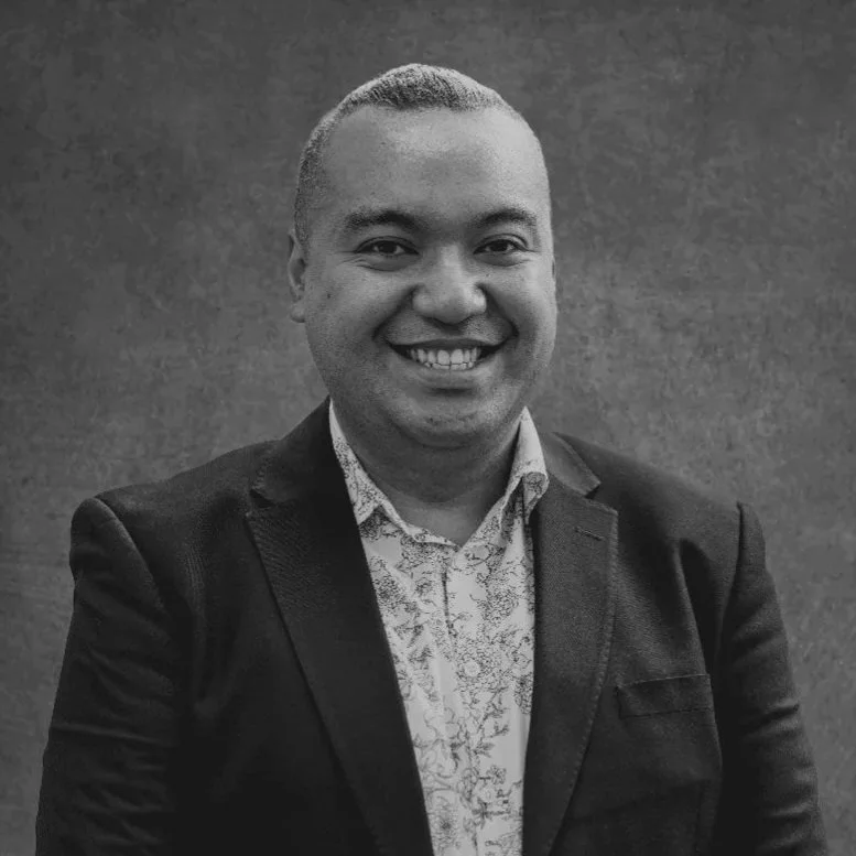 Black and white portrait of a smiling man in a suit with a floral shirt against a plain background.