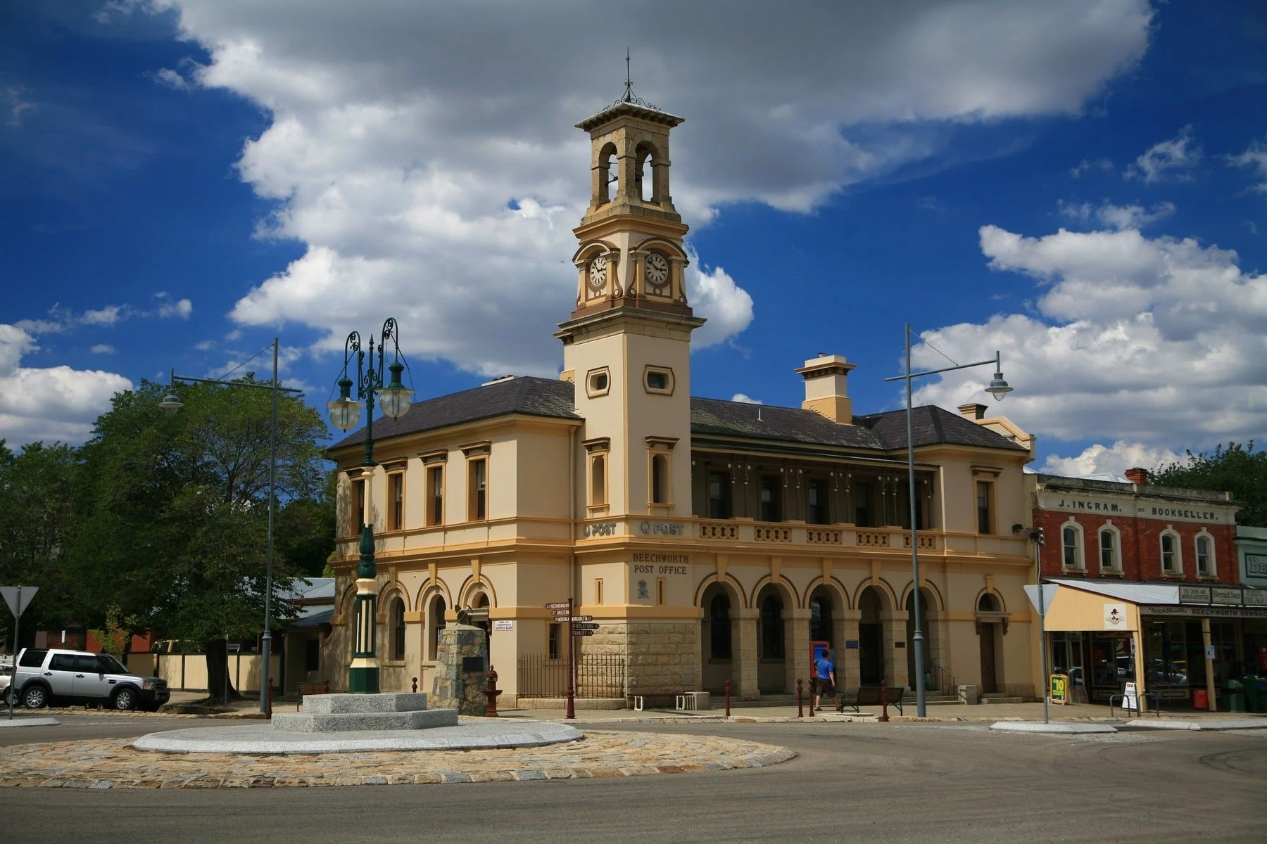A historic building with a clock tower, labeled as Beechworth Post Office, featuring arched windows and a beige facade, situated on a city street with pedestrians and street lamps.