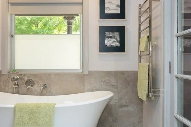 A bathroom with a freestanding bathtub, a window showing green trees outside, and a towel rack with yellow towels.
