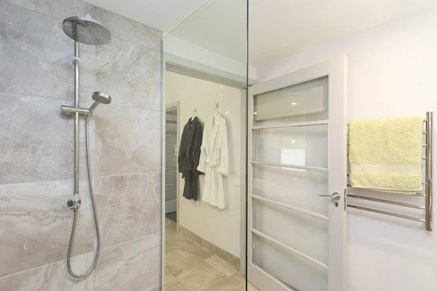 Shower area with gray tiled wall, sliding door with frosted glass, and hanging towels in a bathroom.