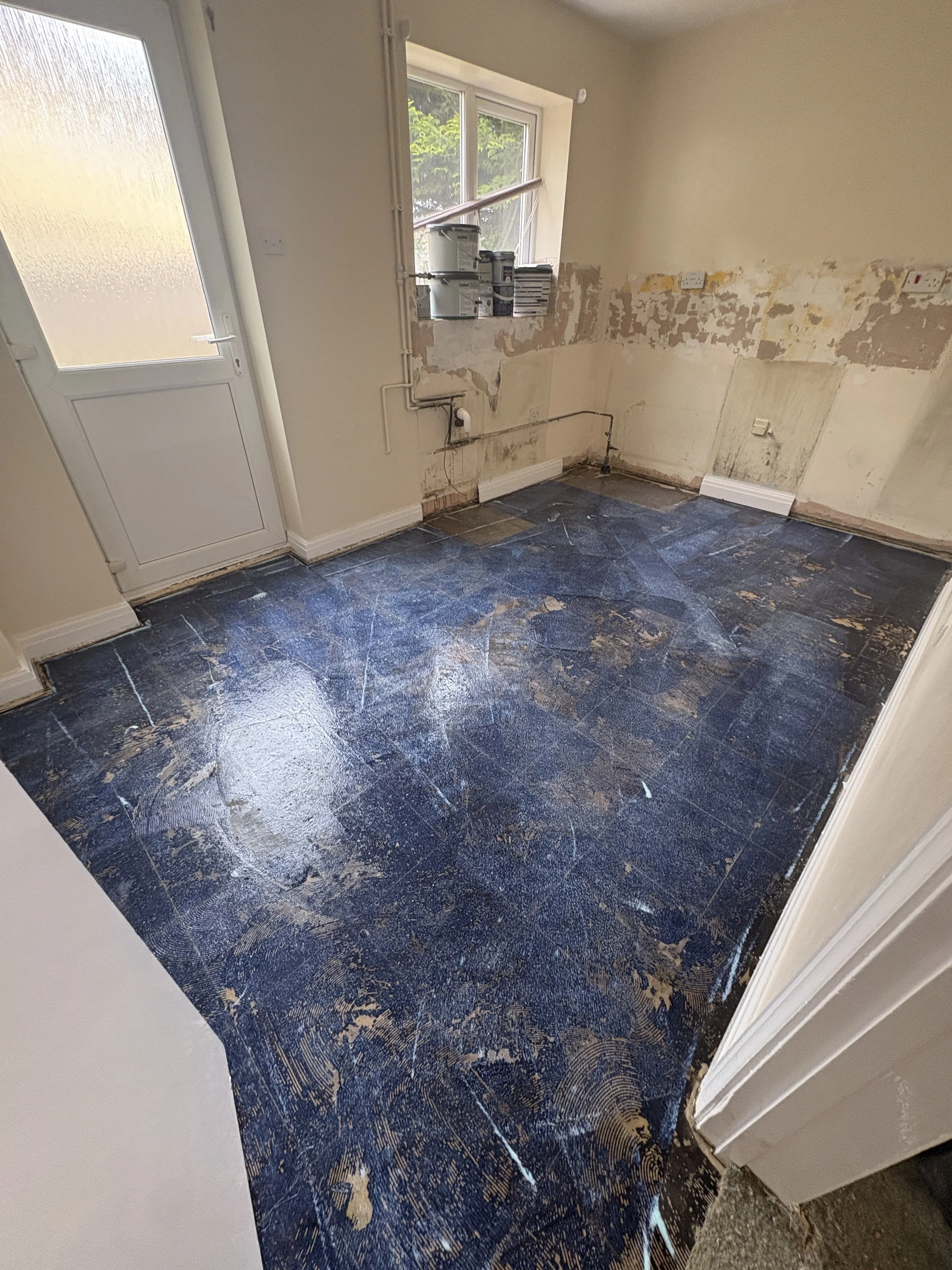 Room under renovation with partially painted walls, floor covered in protective plastic sheeting, and painting supplies on window sill.