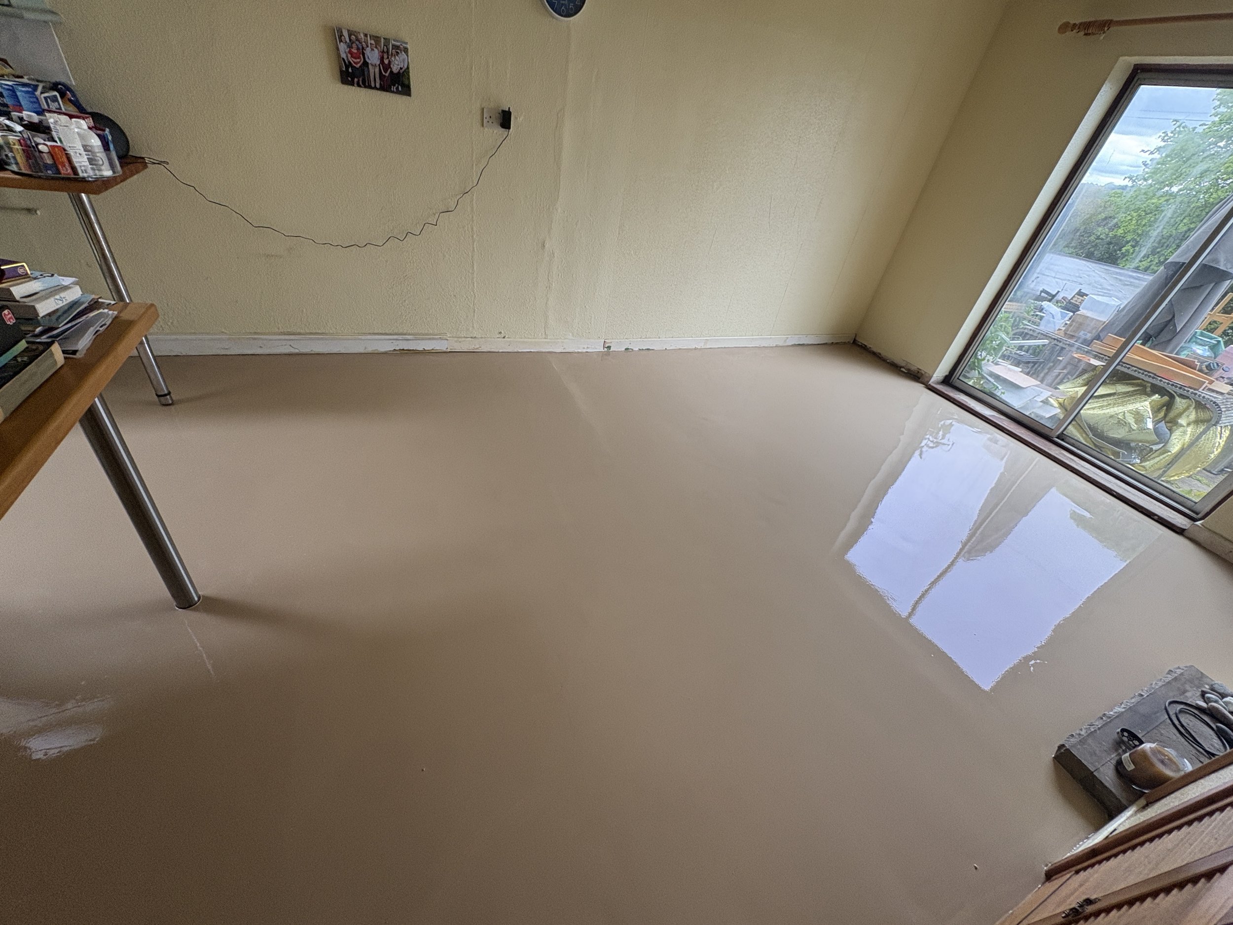 Empty room with a glass sliding door leading to a porch, with some storage items visible outside. The room has beige painted walls, a beige floor, and a family photo on the wall.