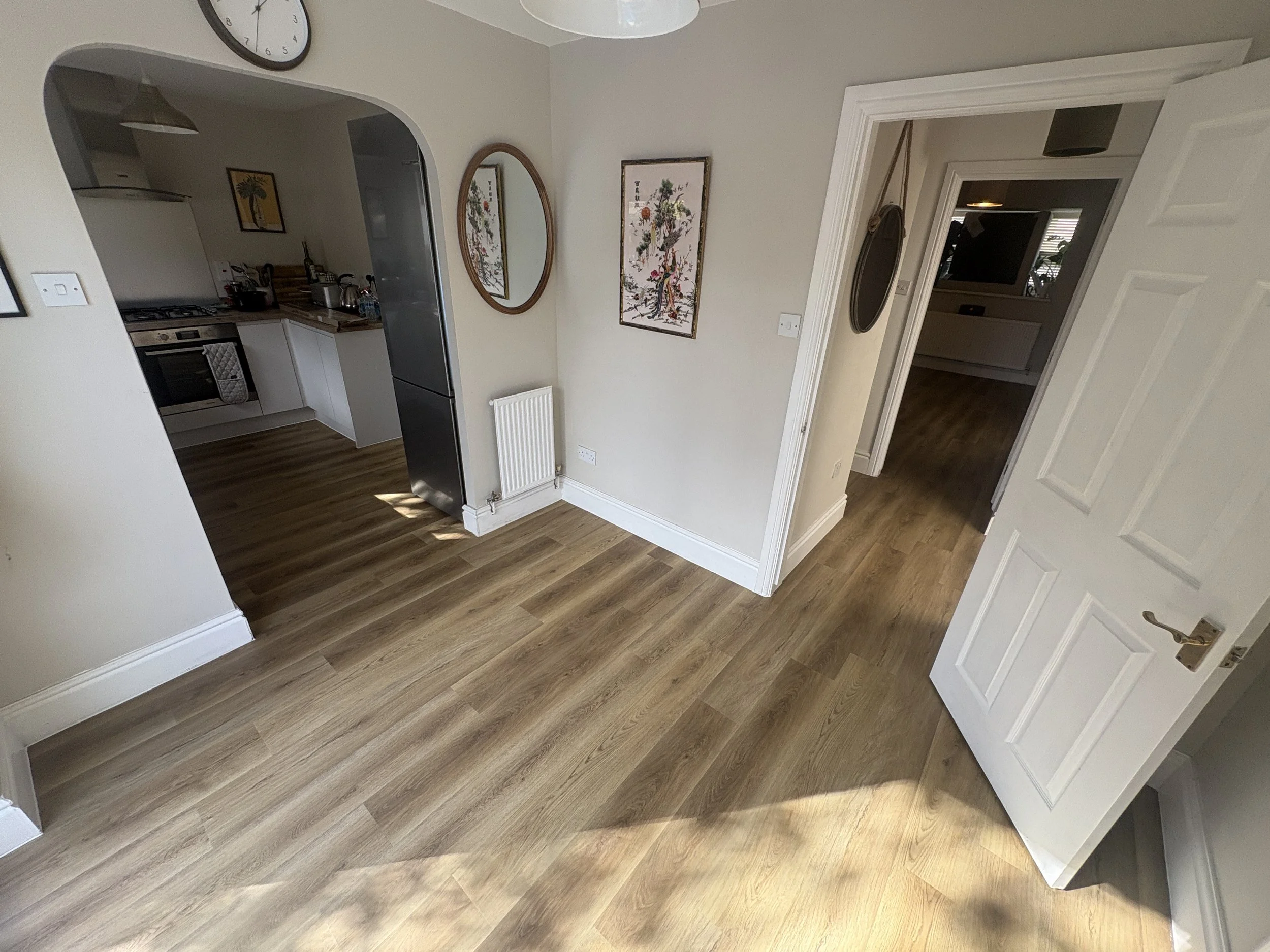 Living room with beige walls, wooden flooring, framed artwork, and a white door open to a hallway.