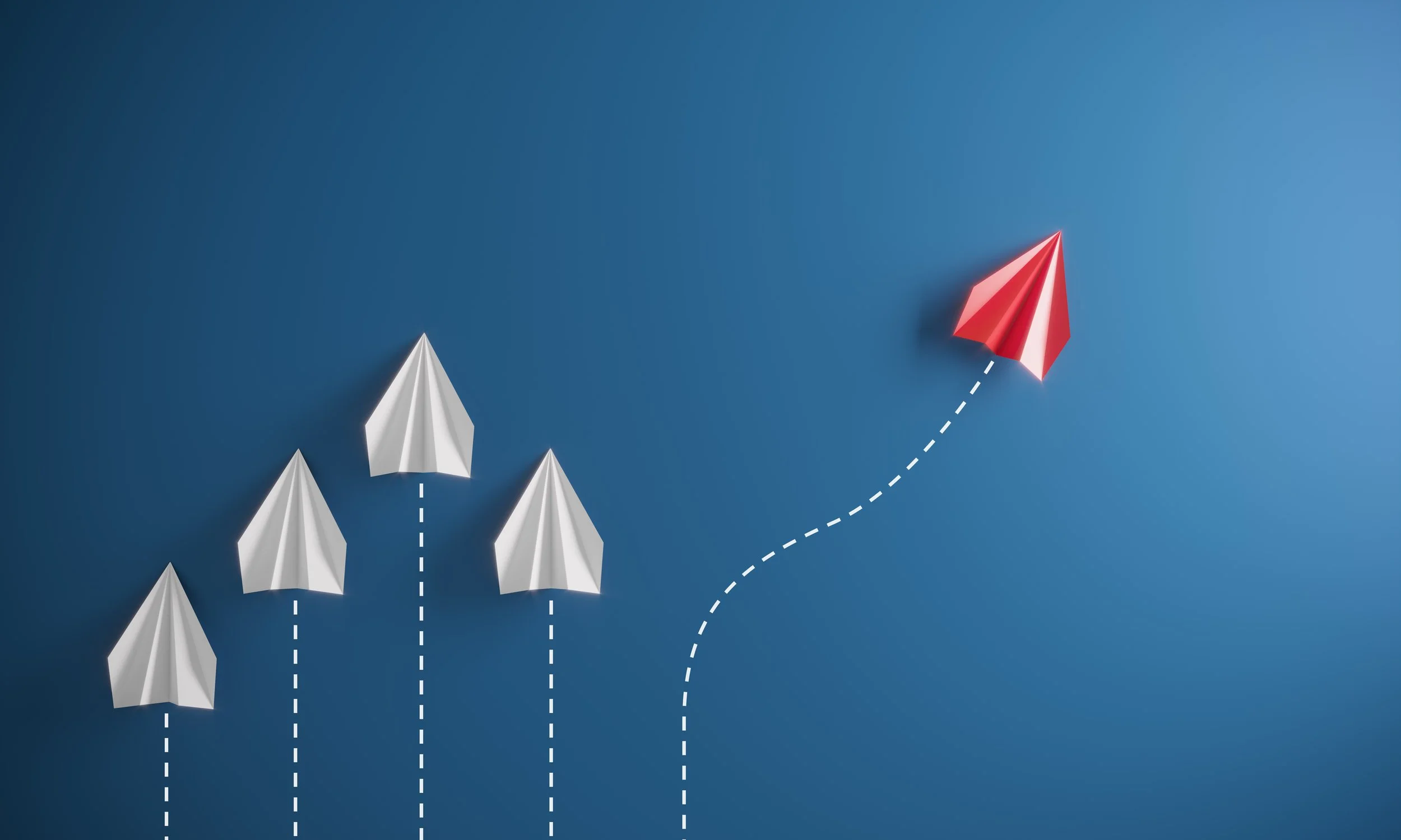 Five paper airplanes, four white and one red, arranged on a blue background with dashed lines indicating movement, with the red airplane following an upward curve.