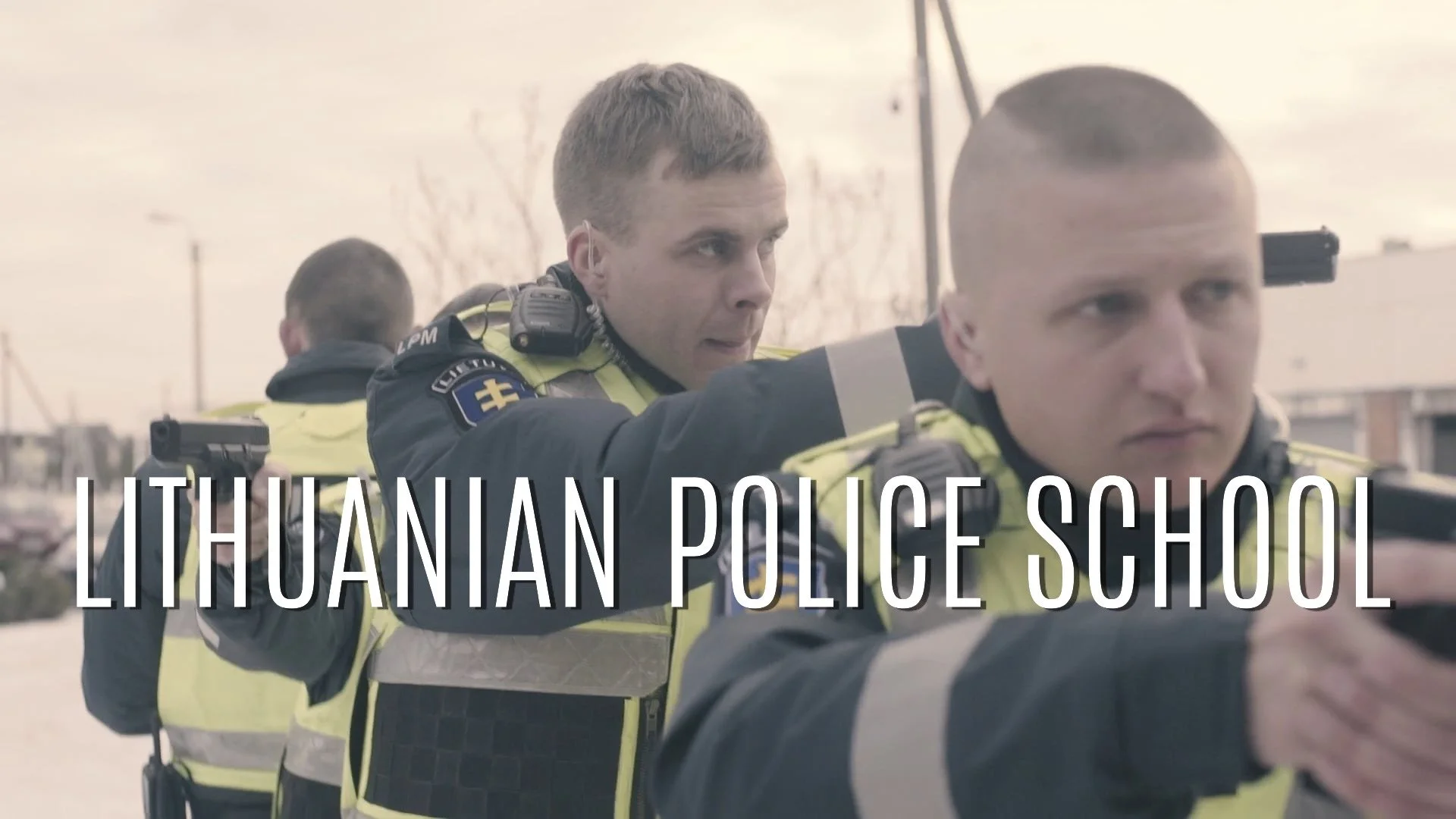 Three Lithuanian police officers in uniform aiming guns during a training session or operation.
