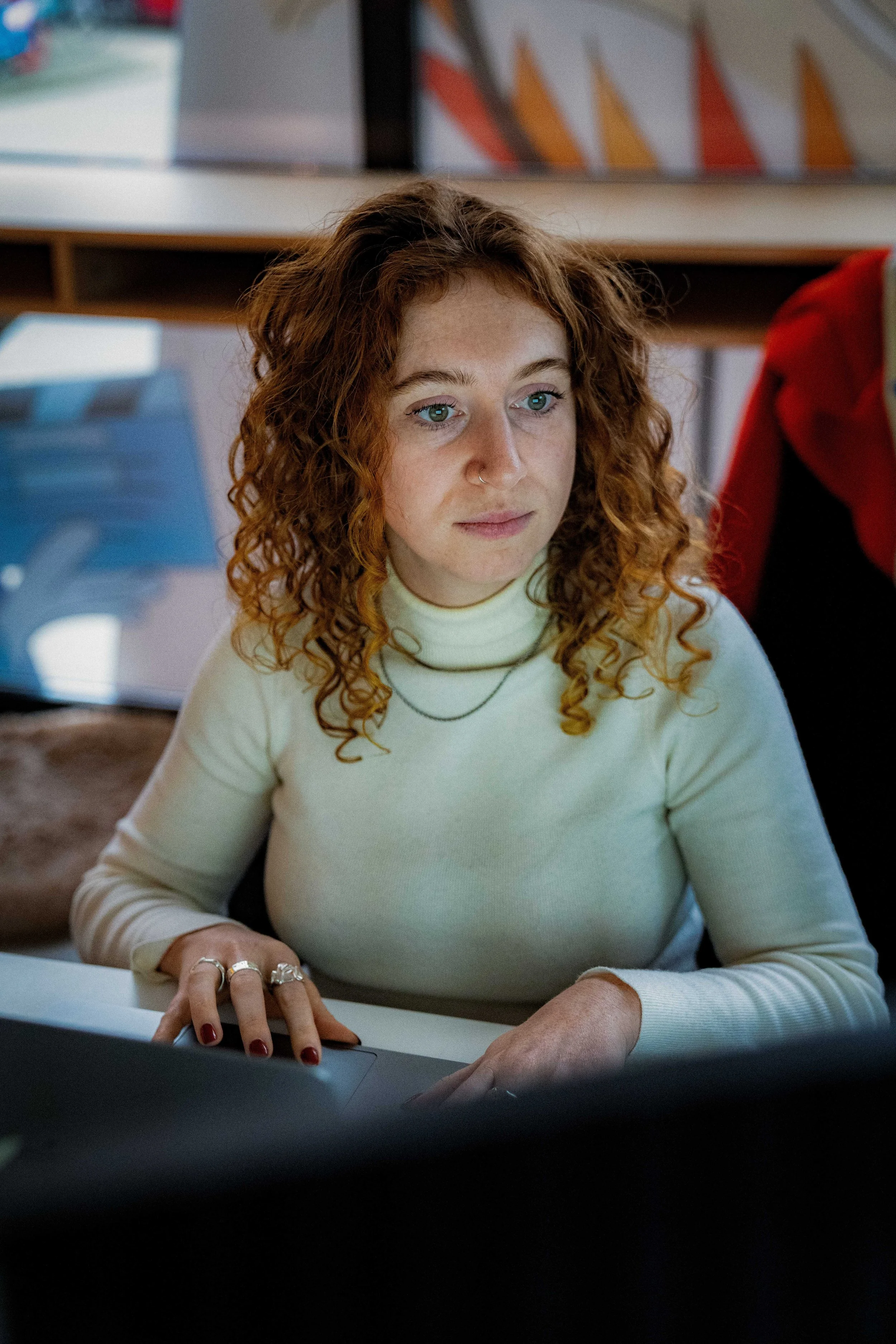 Vrouw met rood krullend haar in een witte trui werkt achter een computer.