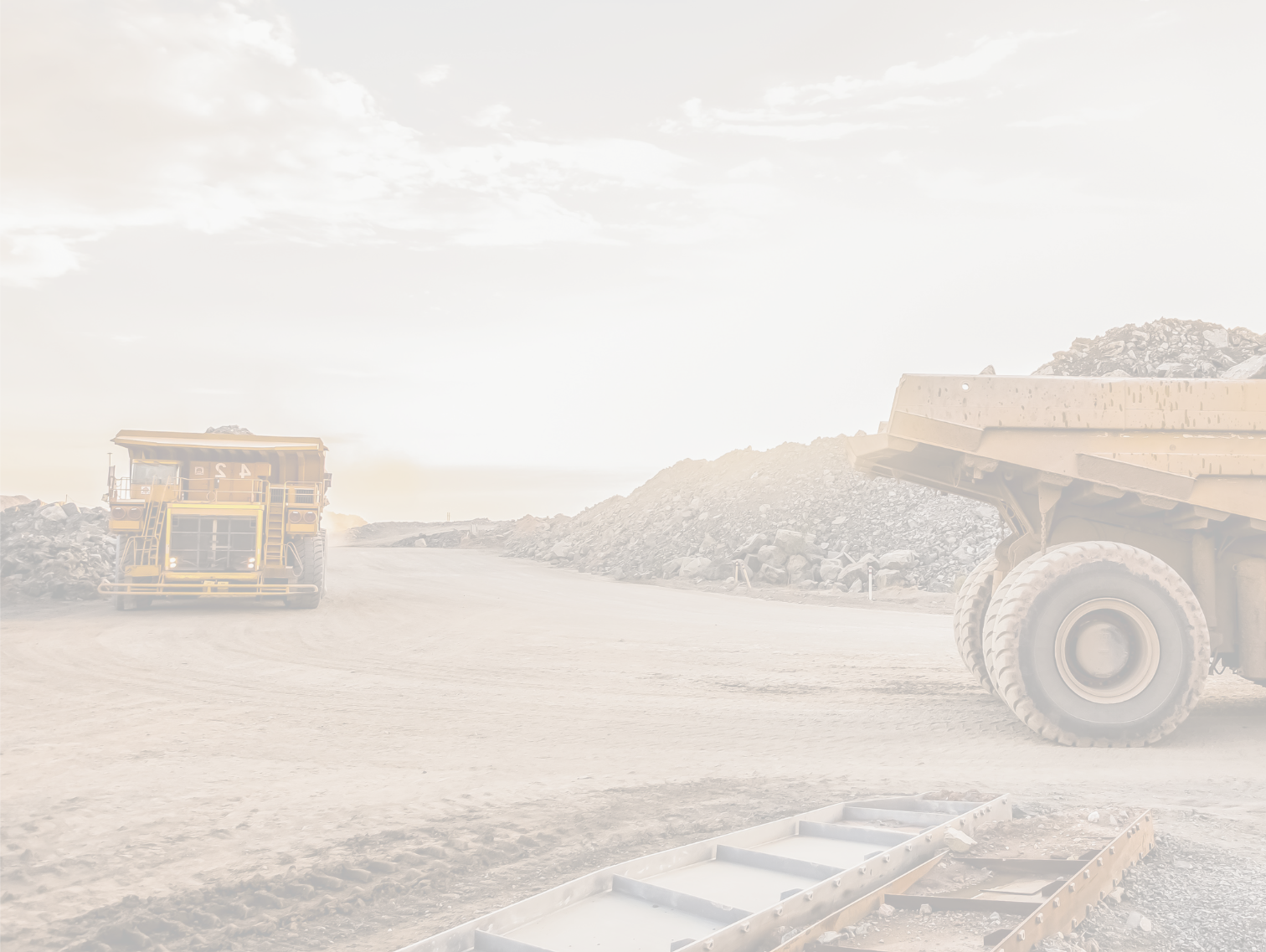 Construction workers with large dump trucks, piles of rocks, and dirt under a partly cloudy sky.