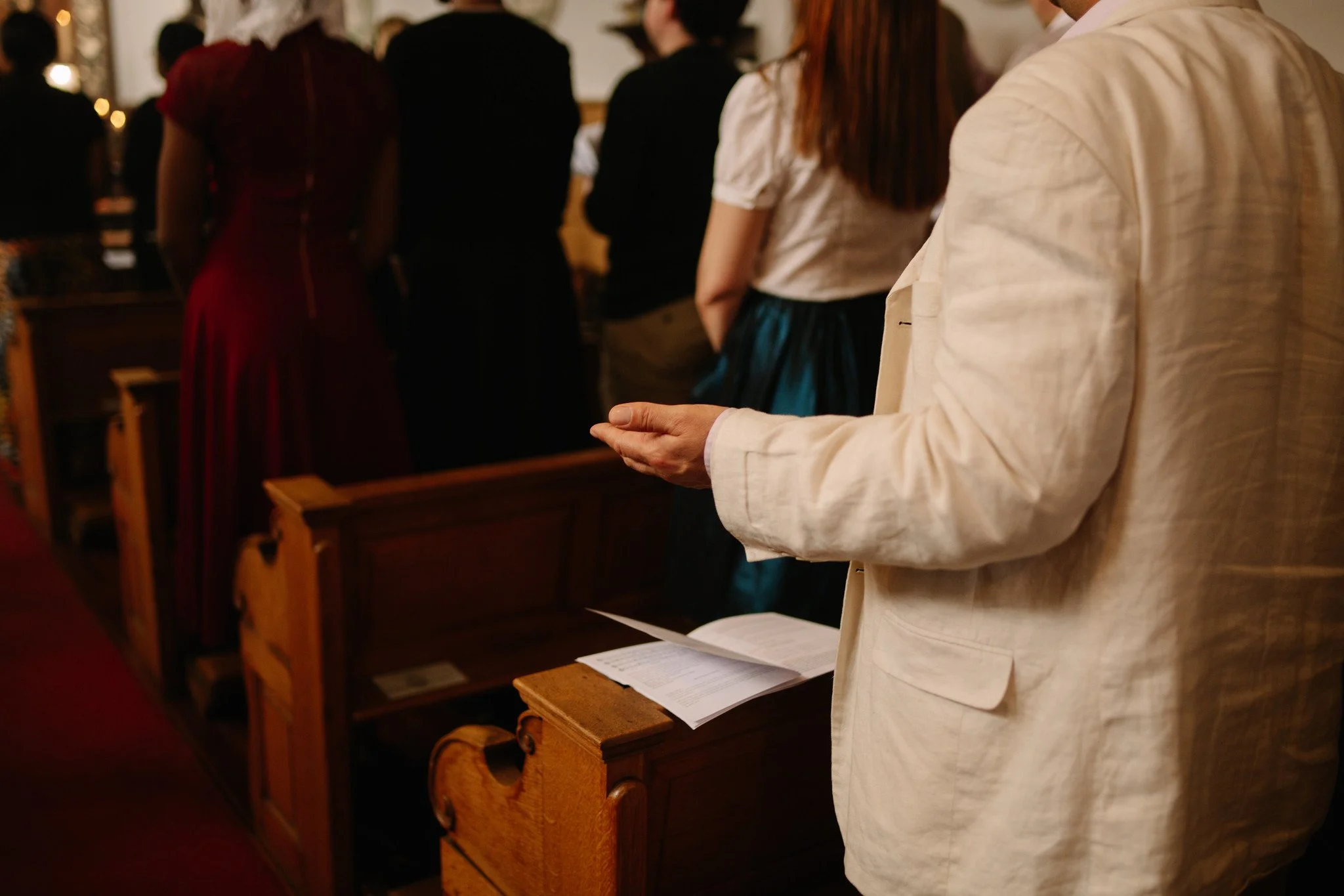 People standing and praying in a church during a mass, with mass book on the pew.