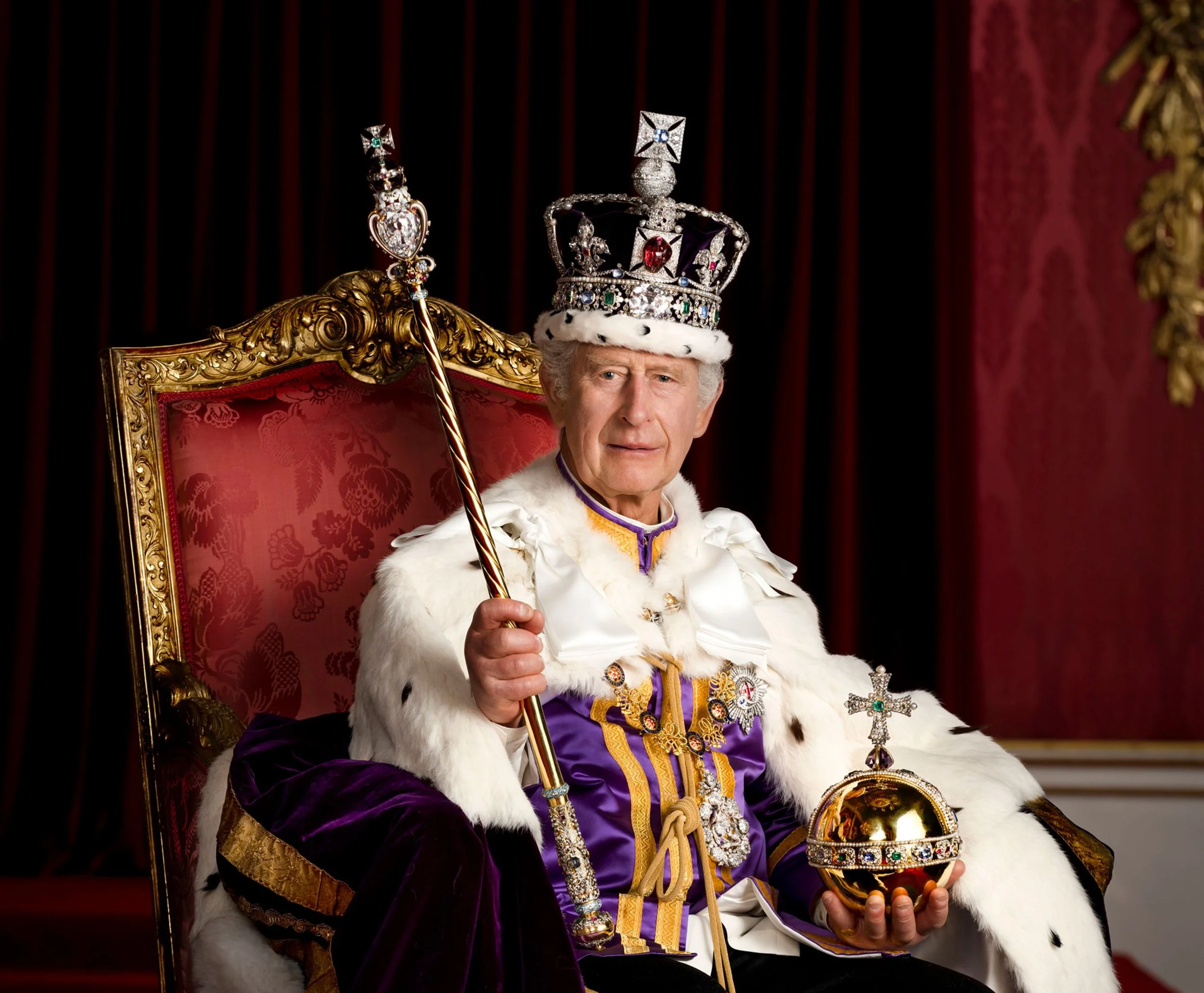 King Charles wearing a crown, robes, and sitting on a regal throne, holding a scepter and a golden orb, with a red curtain background.