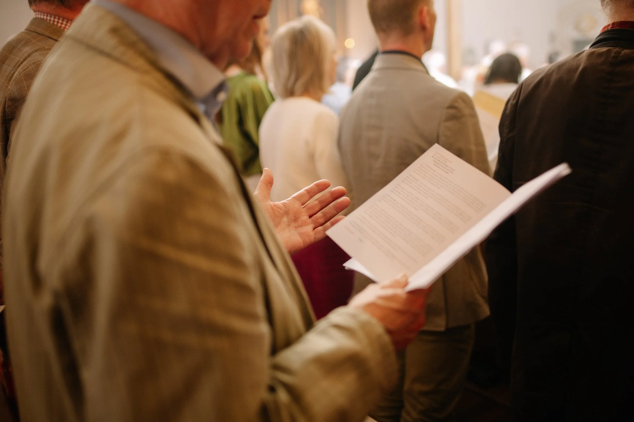 People standing in a church, some reading from a prayer book, attending a mass.