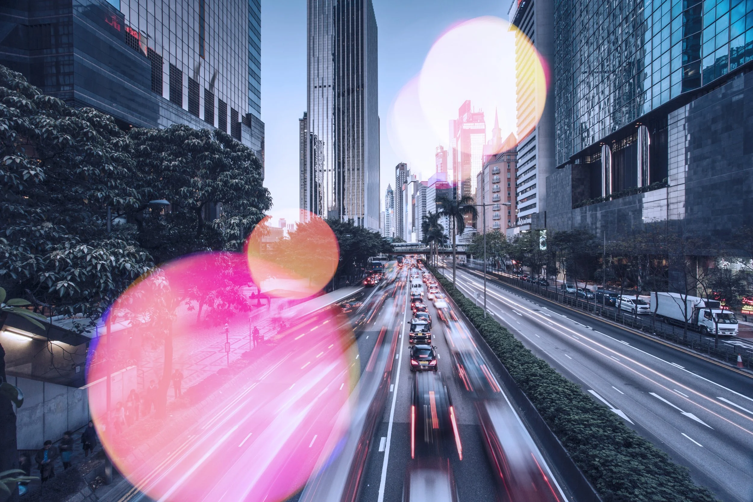 City street with tall buildings, busy traffic, and blurred car lights with rainbow-colored bokeh