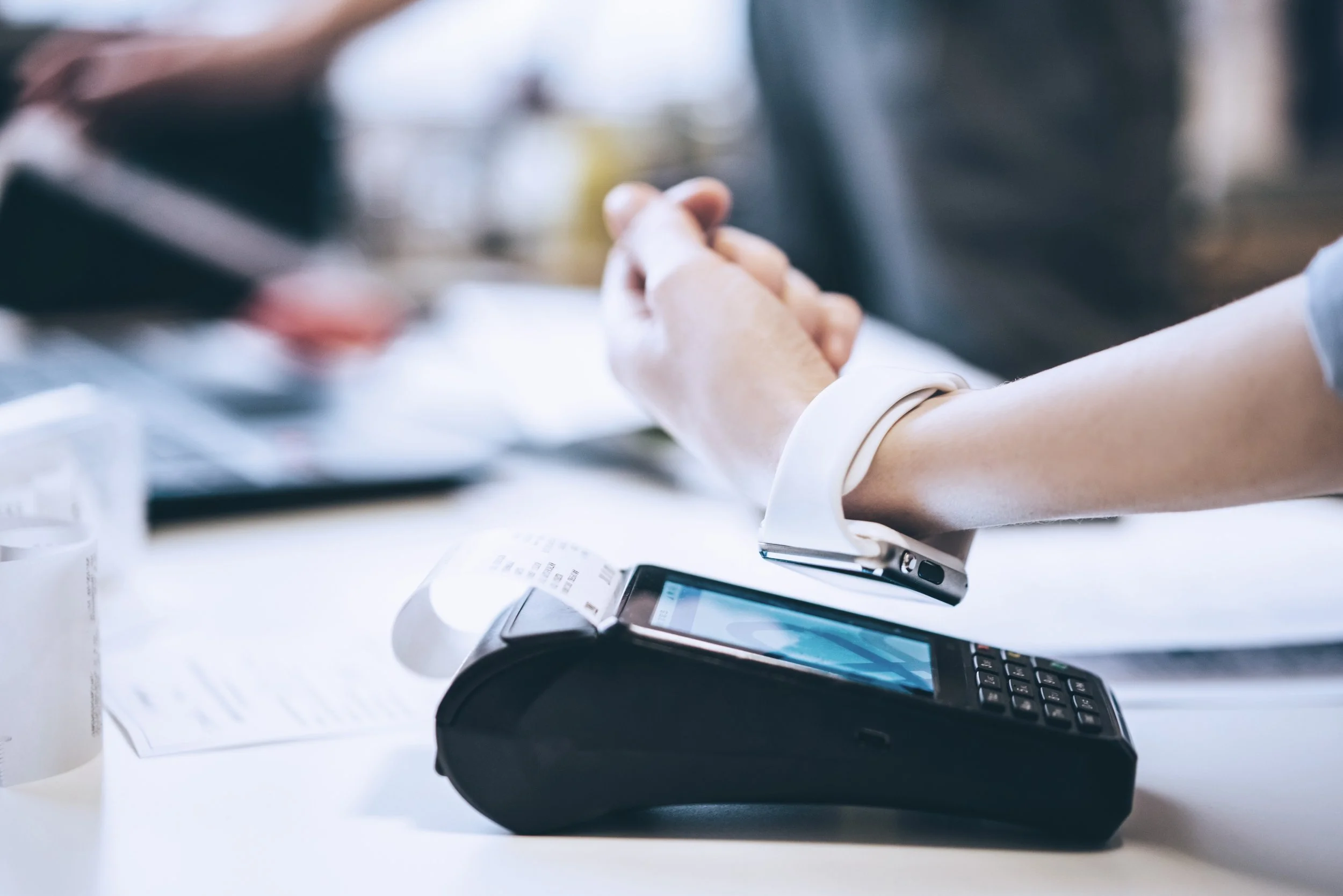 Close-up of a person holding hands on a counter, with a point-of-sale terminal and receipt paper on the table, in a retail or restaurant setting.