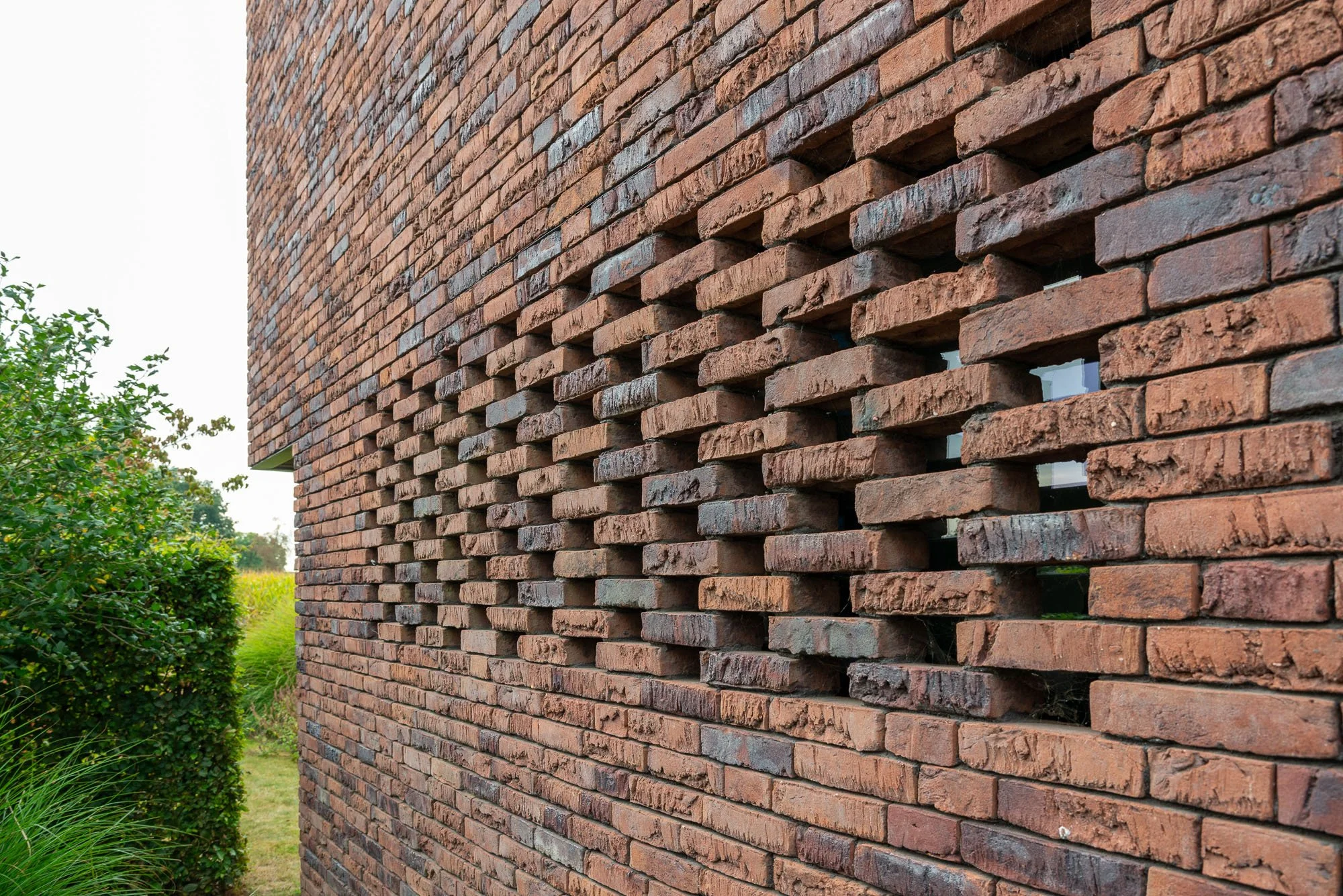 Een rode bakstenen muur met enkele horizontale openingen, ontworpen door Gert Anthonissen Architect, Noorderkempen, Brasschaat, Essen, Kalmthout, Kapellen, Brecht, Rijkevorsel, Malle, Hoogstraten, Merksplas, Schilde, Schoten, 's-Gravenwezel, Sint-Job