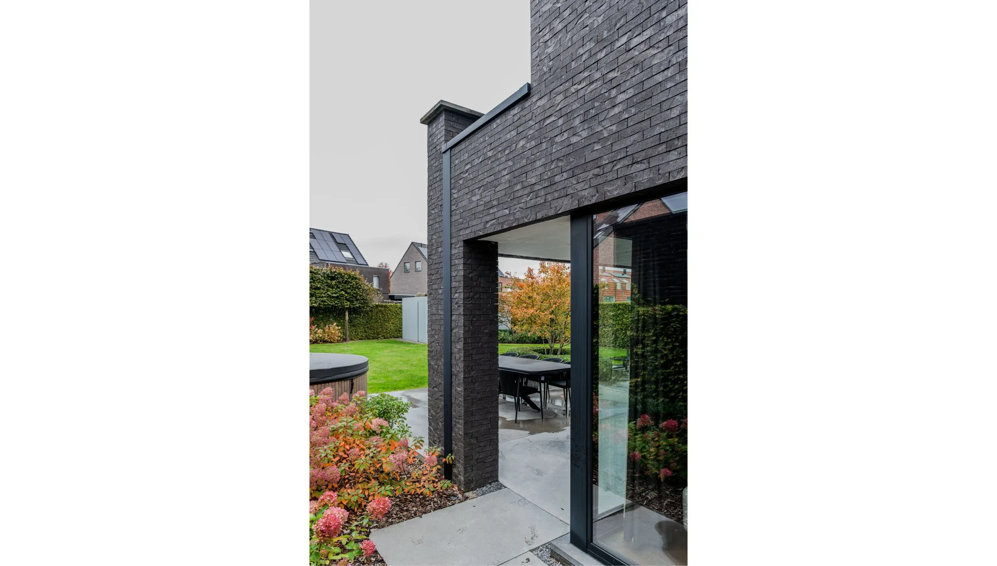 Moderne tijdloze woning met donker bakstenen gevel en grote glazen schuifdeur, uitzicht op een tuin met groen gras. Gert Anthonissen Architect