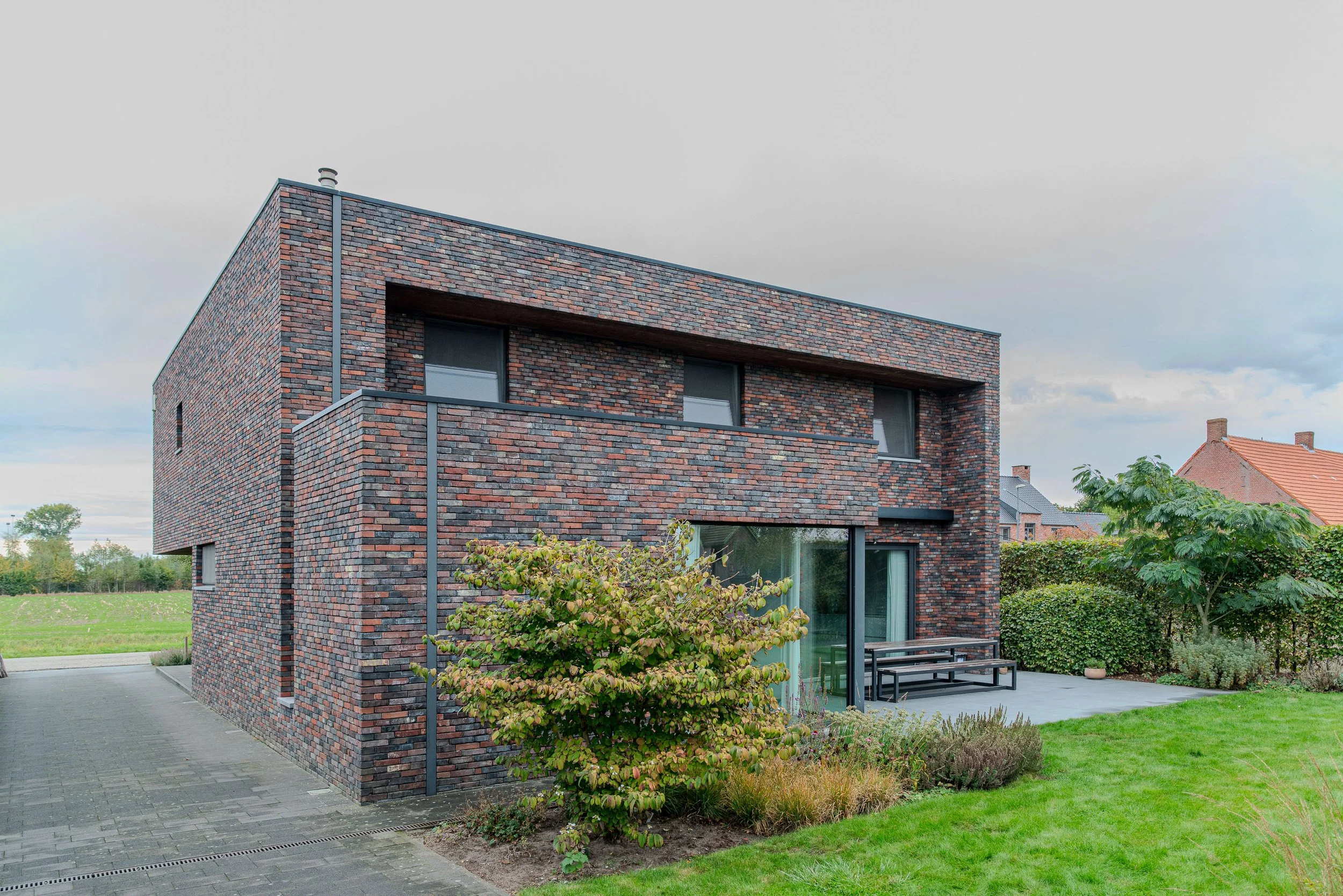Moderne woning met bakstenen gevel en grote ramen, aangelegd tuin. Architectuur Noord Antwerpen, Noorderkempen, Gert Anthonissen Architect.