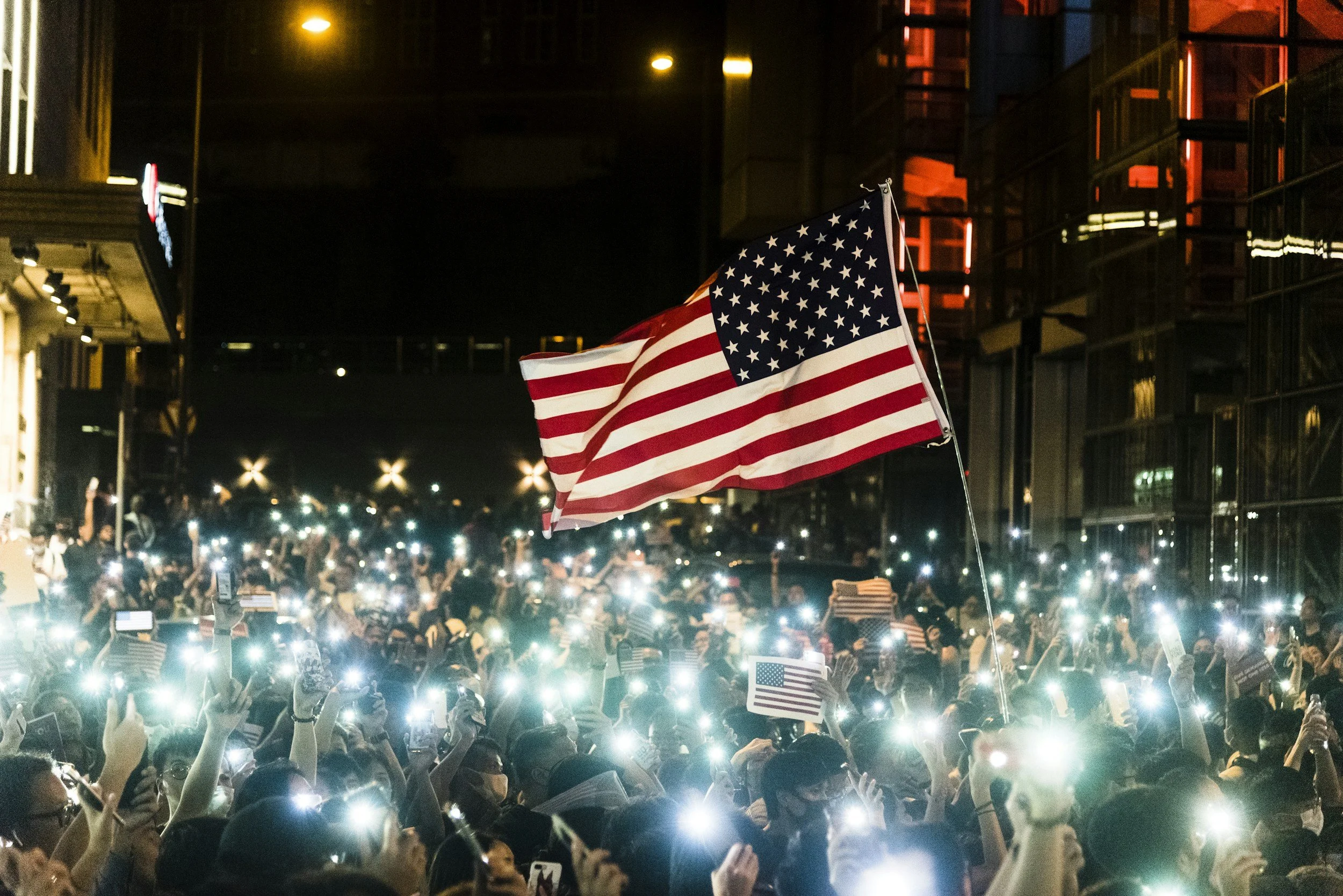Crowd of people at night holding up lights and waving American flags in celebration.