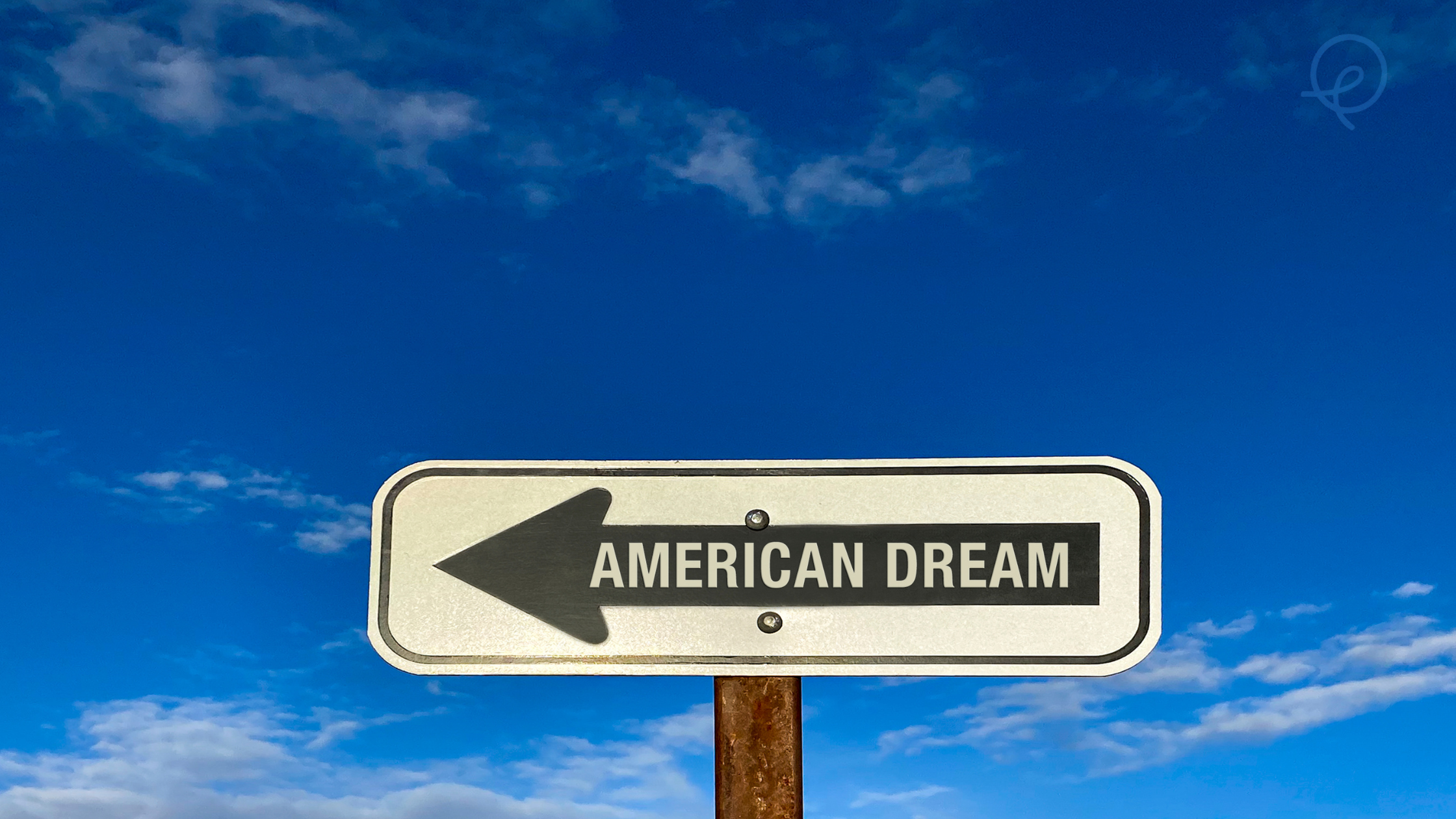 A road sign with an arrow pointing to the left that reads 'American Dream' against a blue sky with some clouds.