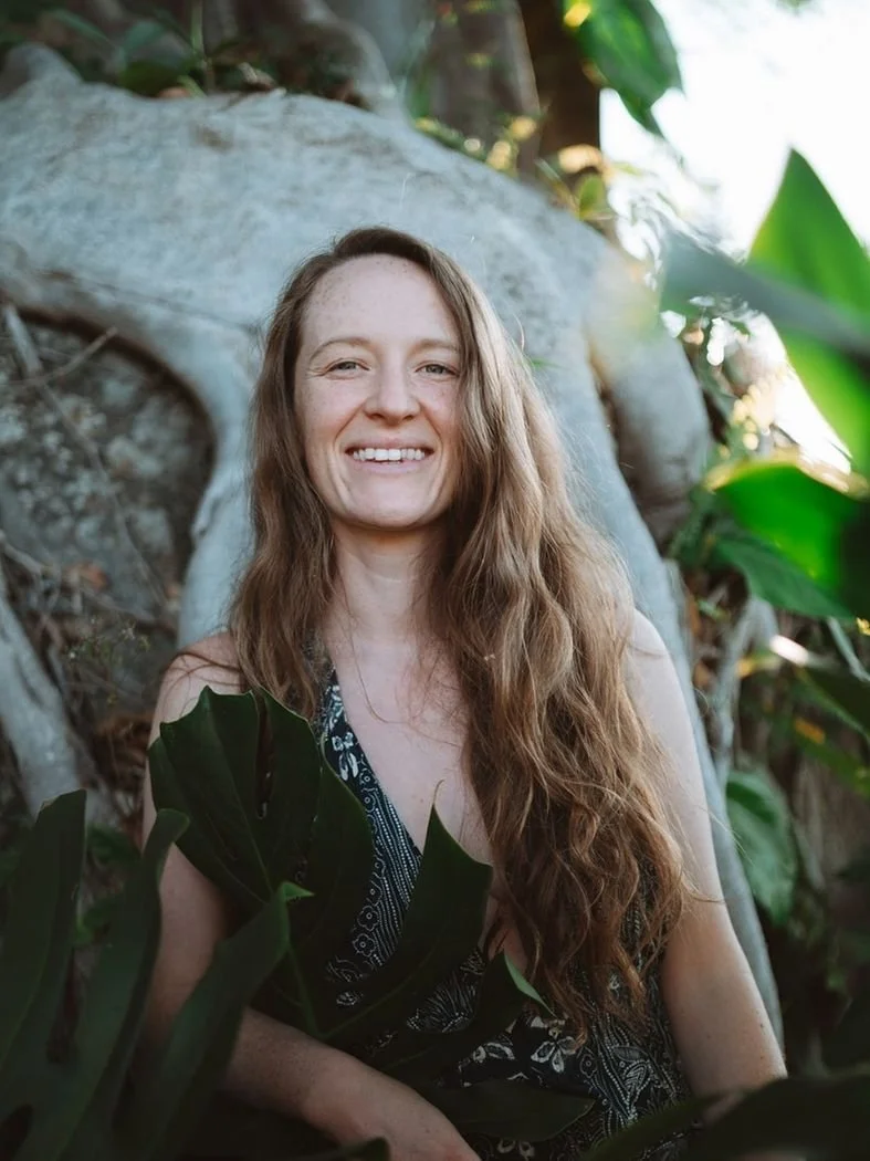 A woman with long, wavy brown hair smiling outdoors, teaching evolutionary astrology.