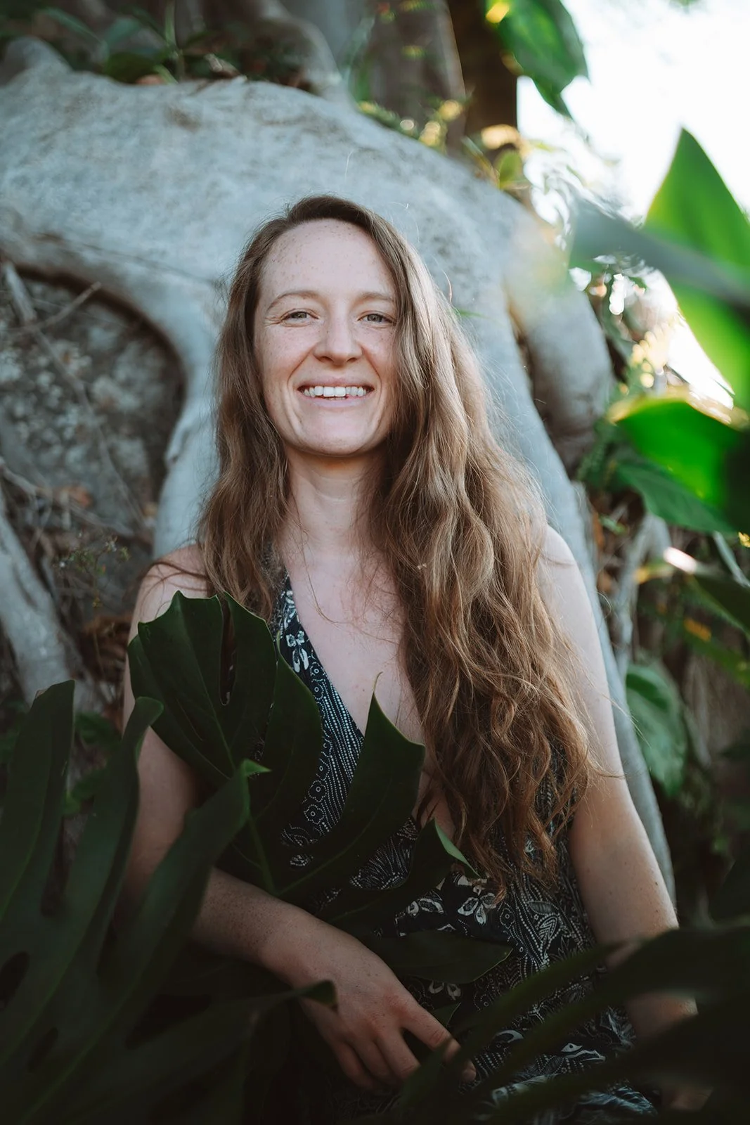 A woman with long, wavy red hair smiling outdoors among green plants and rocks teaching Evolutionary Astrology