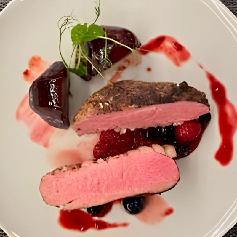 Close-up of gourmet dish with sliced cooked meat topped with colorful fresh vegetables and herbs on a dark plate