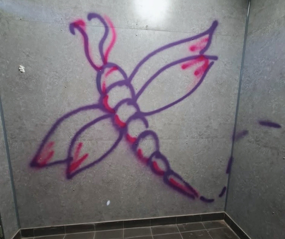 Graffiti of a flower with large leaves and a central stem, drawn with purple outline and highlighted with red accents, on a tiled wall in a corner.