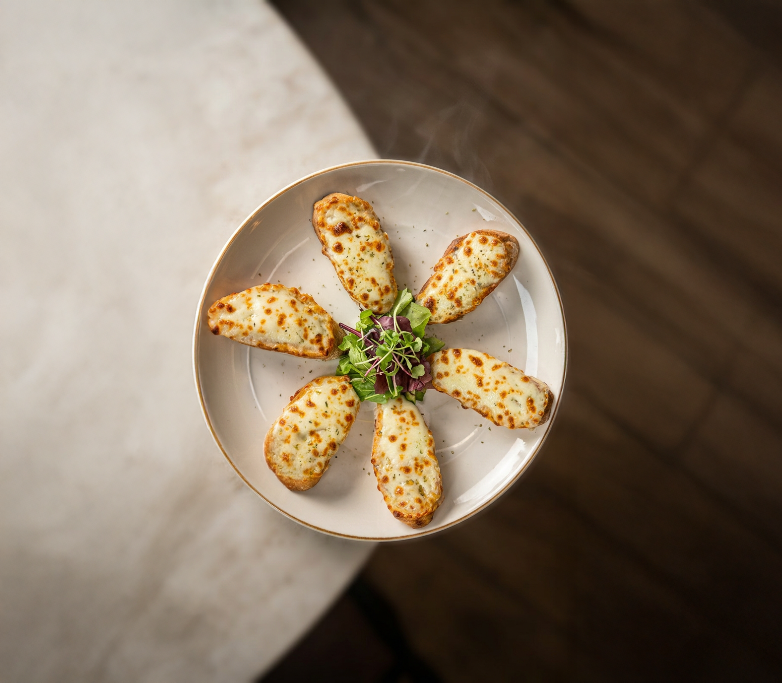 A white bowl with six pieces of cheesy breadsticks topped with melted cheese, garnished with a small handful of leafy greens in the center, placed on a table with a marble and wooden surface.