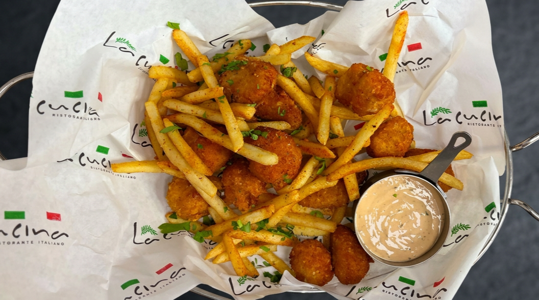 Basket of fried chicken nuggets and French fries with a side of creamy dipping sauce on branded paper liner.