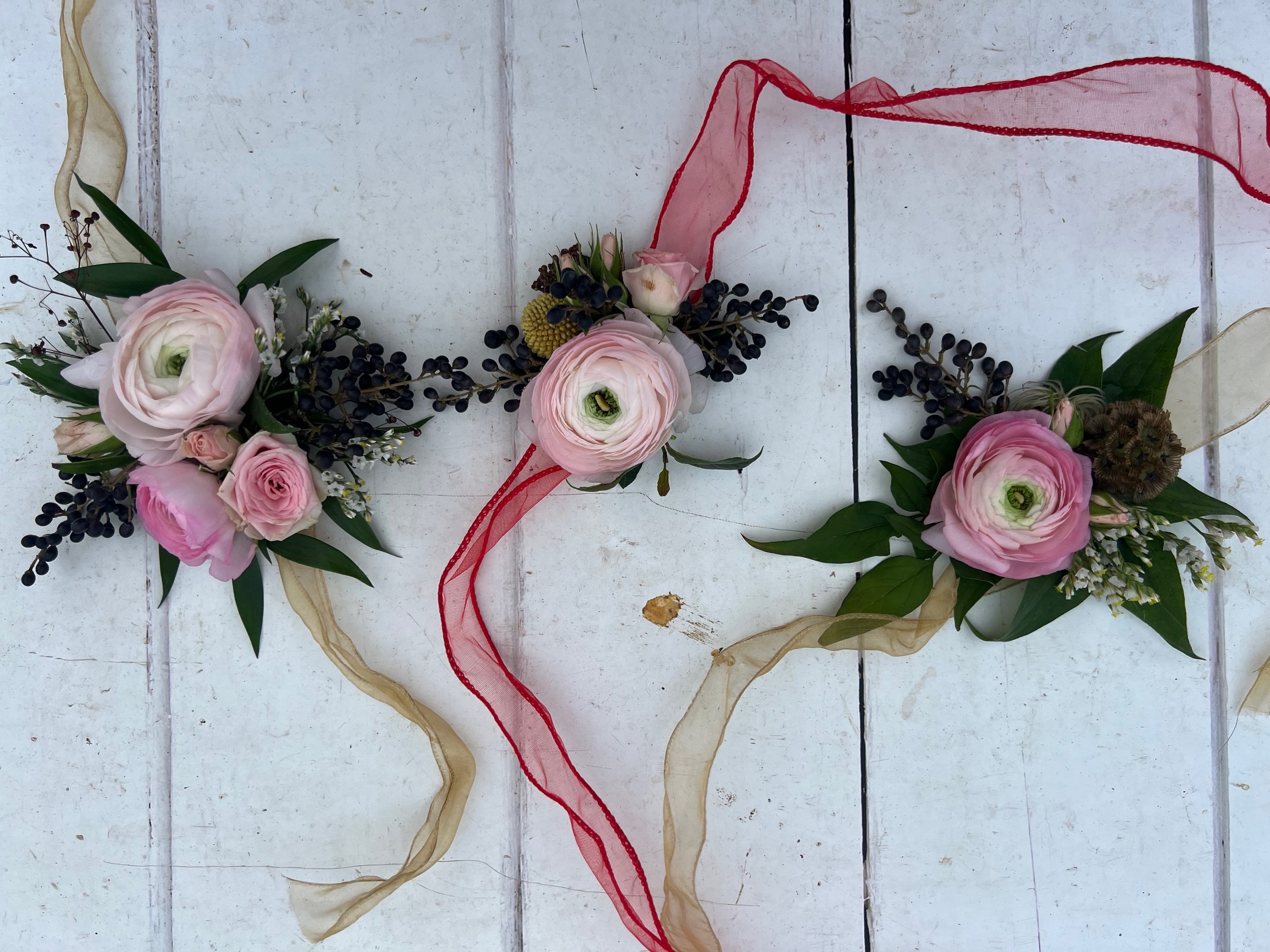 Arrangement of pink and white flowers with greenery, tied with beige and red ribbons on a white wooden surface.