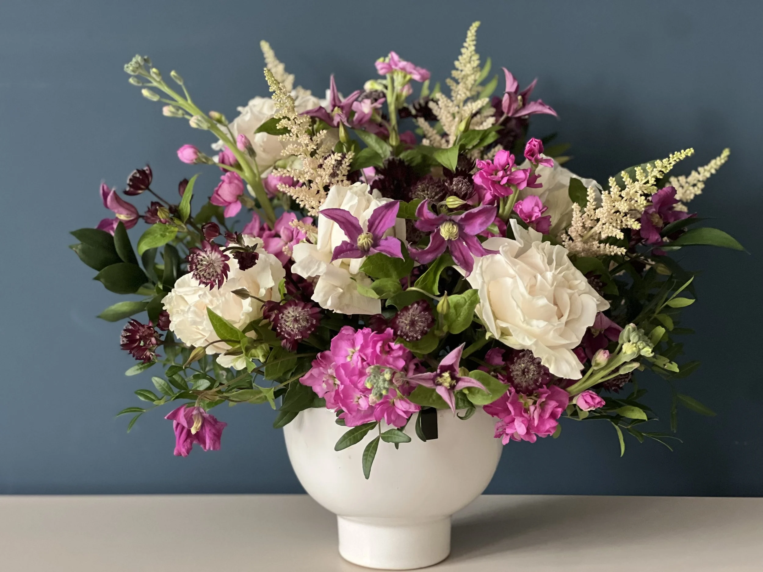 A bouquet of pink and white flowers in a white ceramic vase against a blue background.
