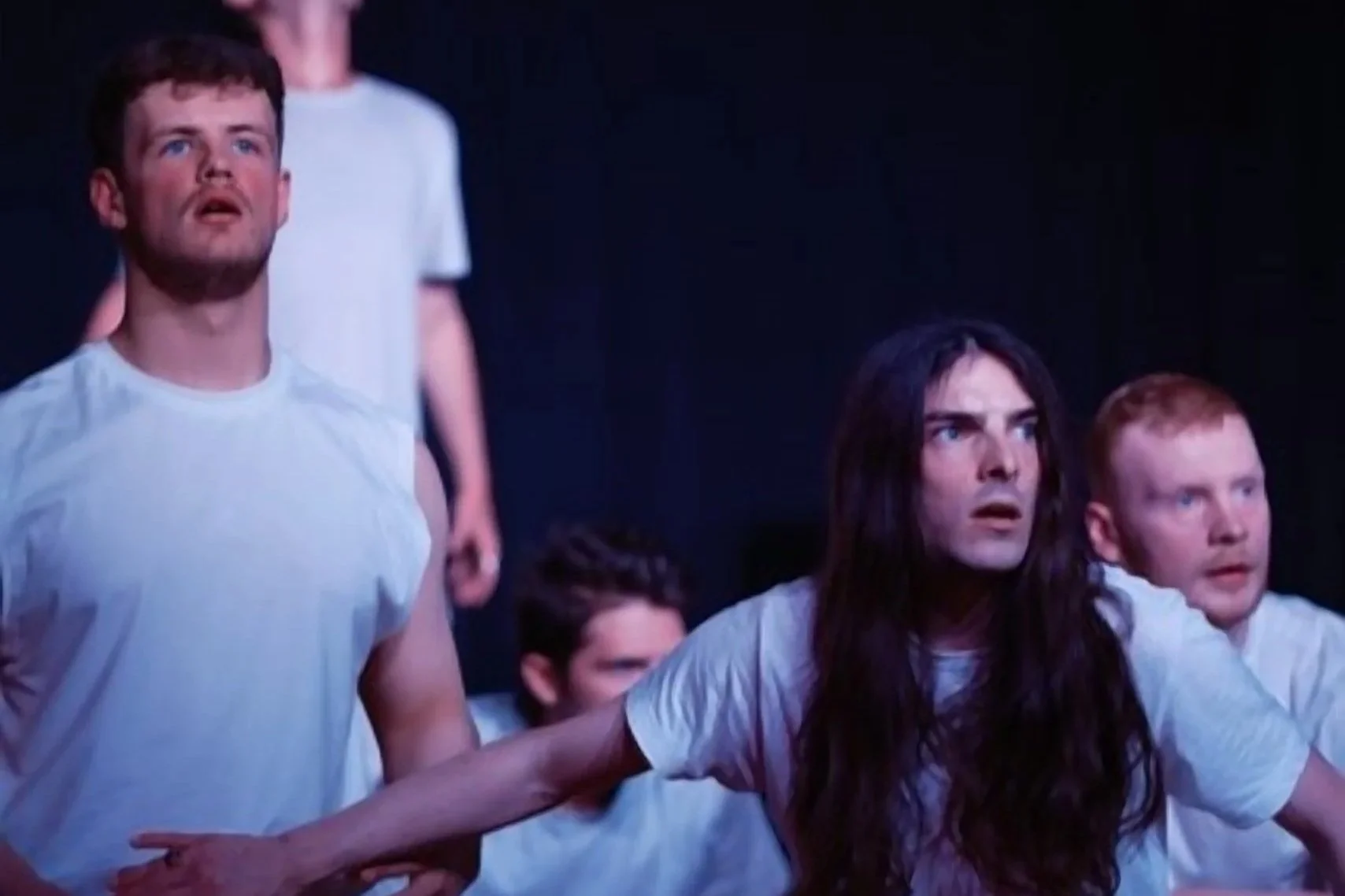 Group of actors in White T-shirts performing on stage with intense expressions.