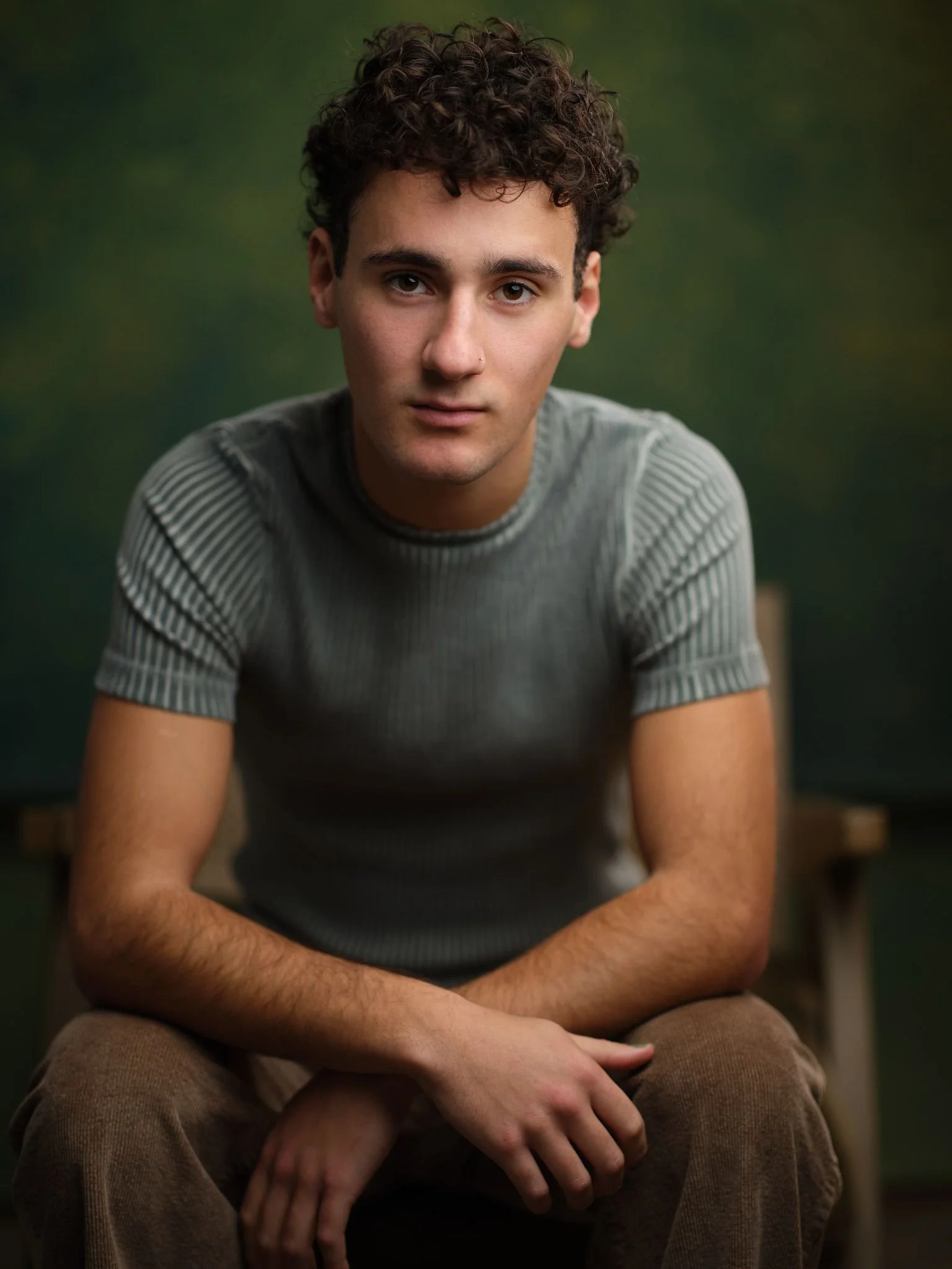 A young man with short brown hair, wearing a green shirt, looking at the camera and smiling slightly.