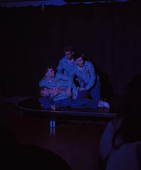 Four children in matching blue and white striped pajamas performing on a small stage with a black curtain backdrop.