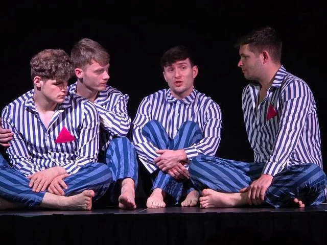 Four young men dressed in matching striped pajamas sitting on a stage, engaged in a discussion.