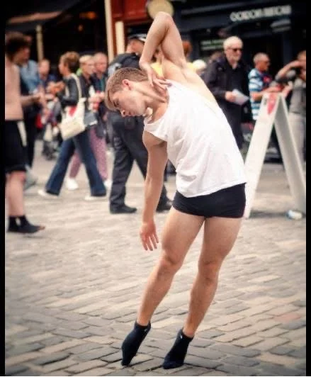 A woman performing a ballet move on their toes in a public outdoor area with onlookers in the background.