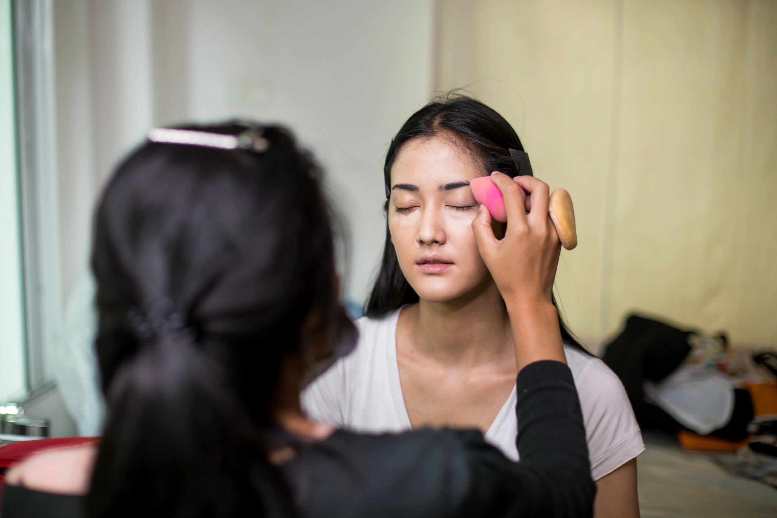 Frau erhält Make-up-Privatsitzung, während sie die Augen geschlossen hat, in einem Innenraum.