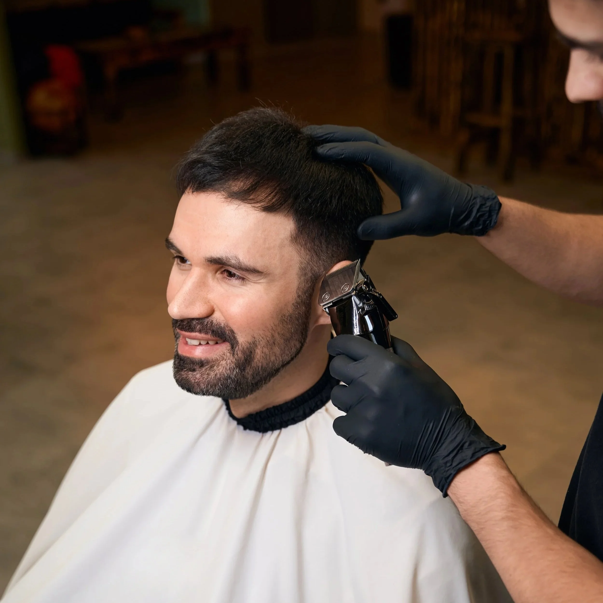 Mann beim Friseurbesuch erhält einen Haarschnitt mit Haarschneidemaschine, während der Friseur schwarze Handschuhe trägt.