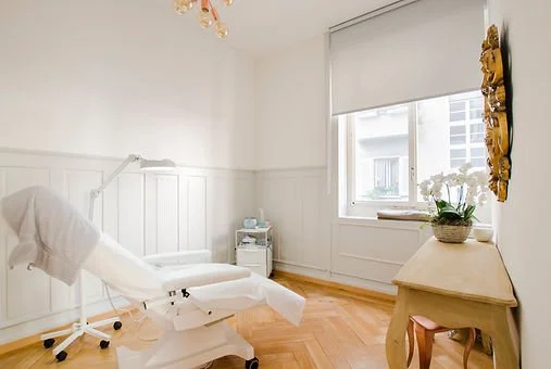 Schön eingerichtetes Behandlungszimmer mit Behandlungsliege, Schreibtisch mit Blumen und Window-View