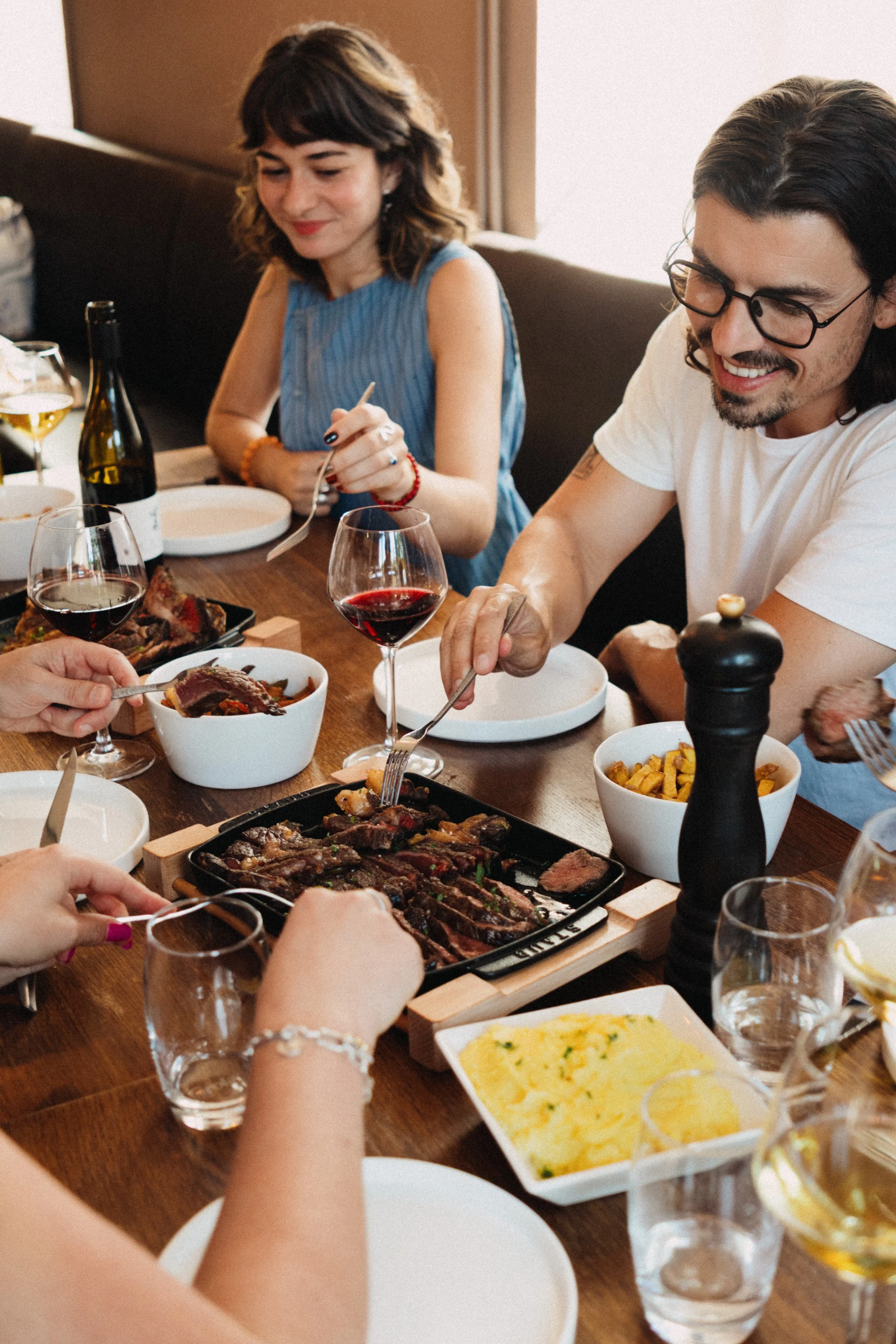 Groupe de personnes partageant un repas avec des viandes, des légumes, du vin et des boissons gazeuses dans un restaurant