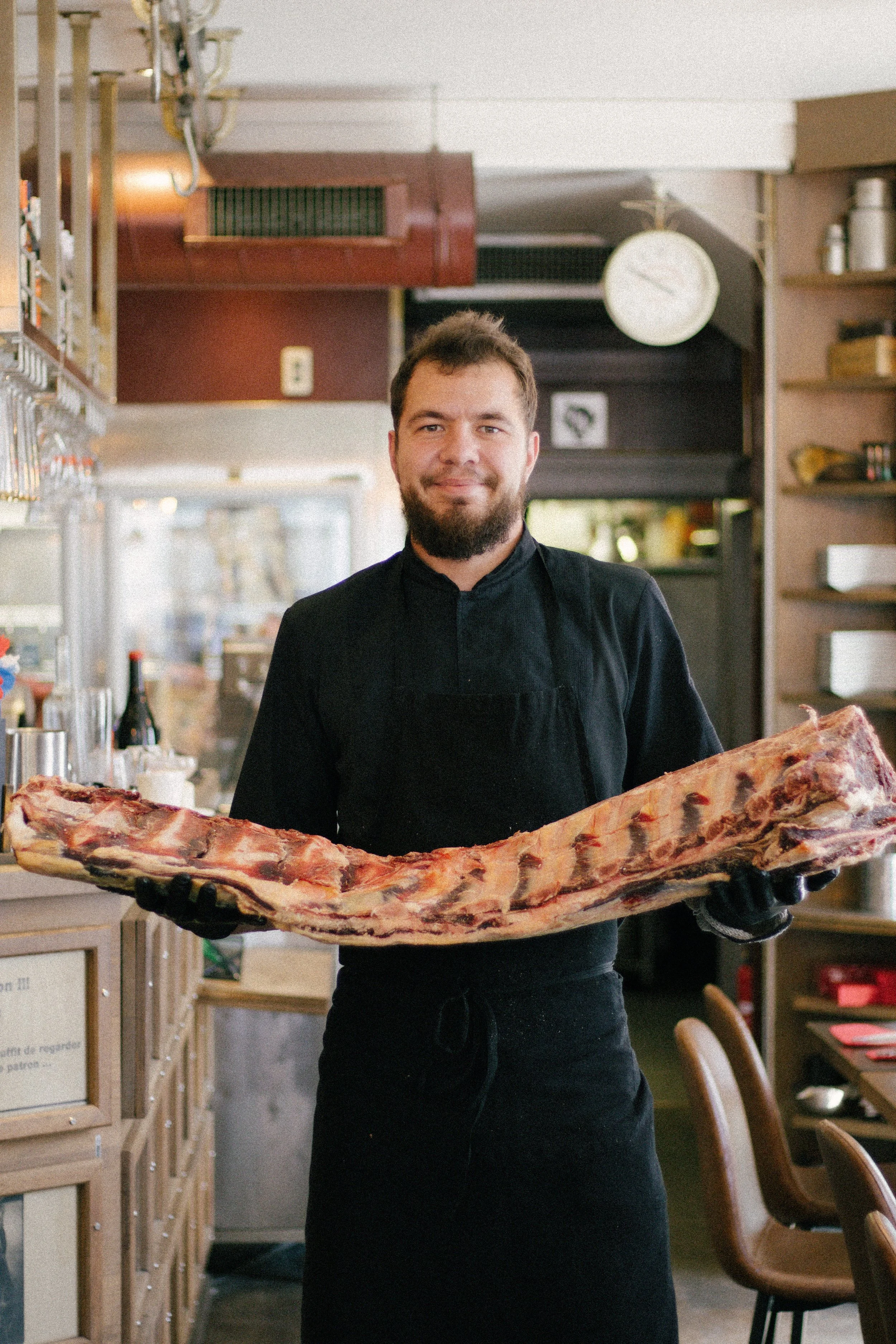 Un homme en uniforme de cuisinier tient une grande pièce de viande dans un restaurant.
