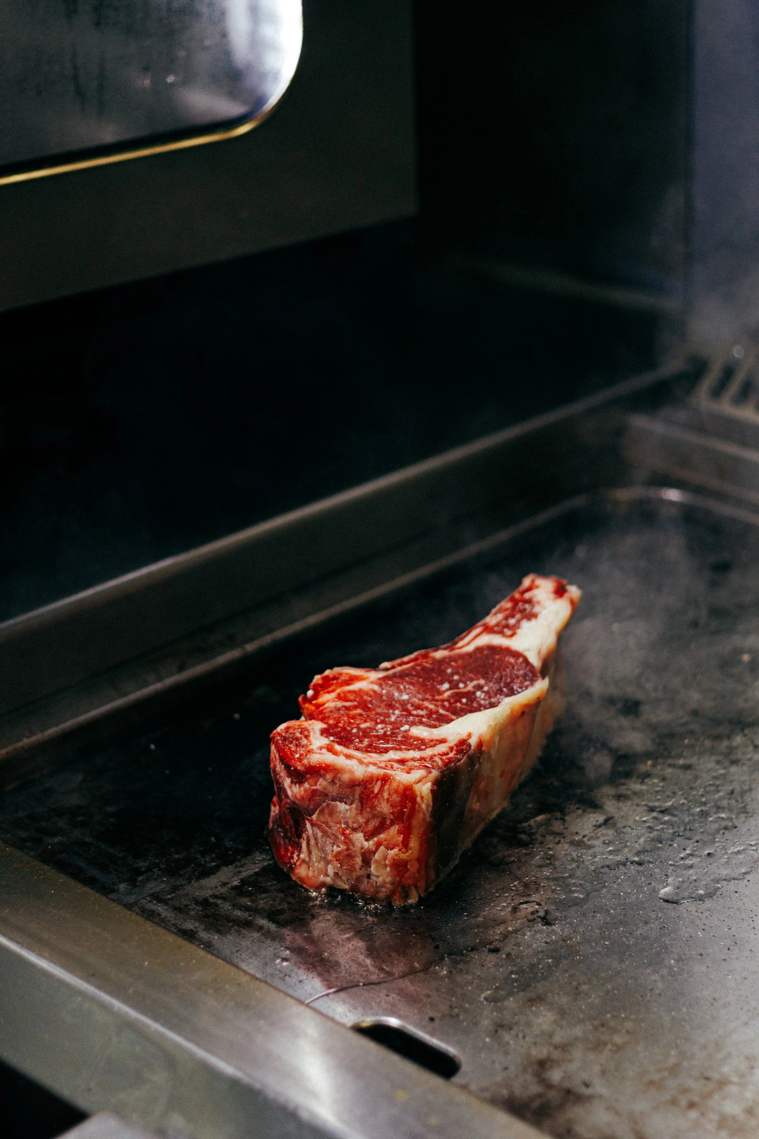 Une pièce de viande rouge, probablement un steak ou un côtelettes, en train de cuire dans un four ou sur une plaque de cuisson en métal.