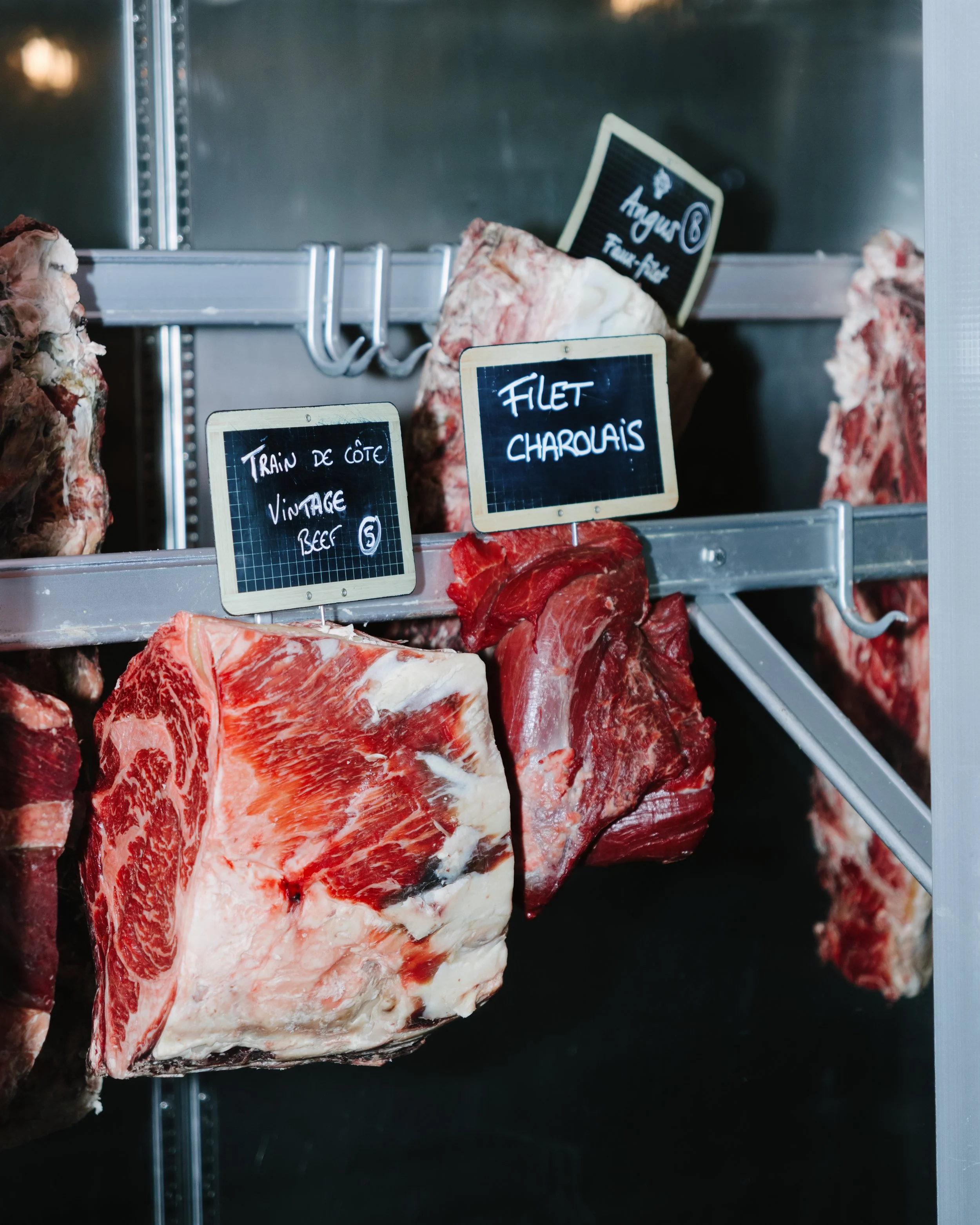 Viande de bœuf coupée en morceaux dans une vitrine, avec des étiquettes indiquant 'Traînu de côte vintage beef' et 'Filet charolais'.