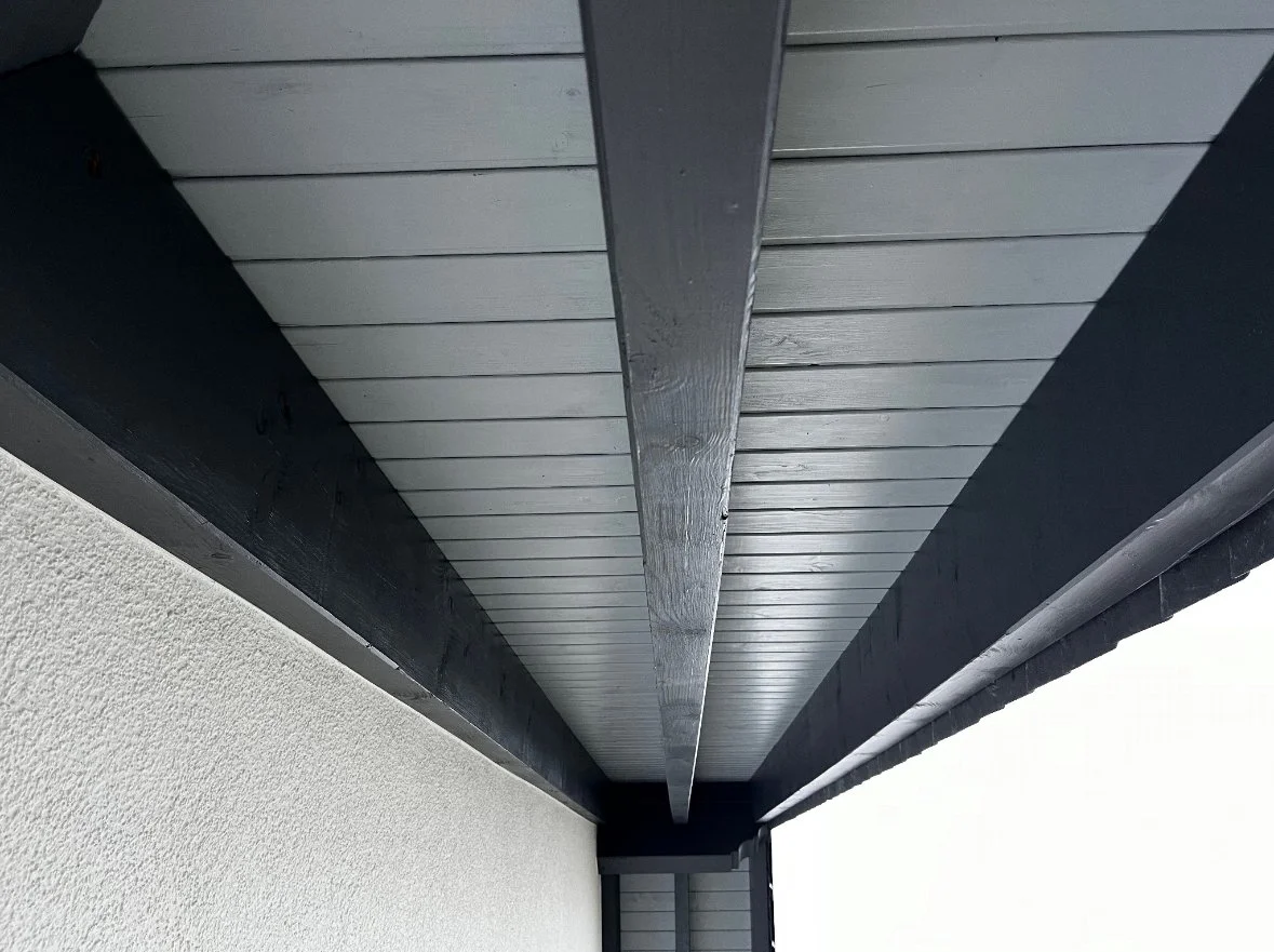 Untersicht eines Dachs mit schwarzen Dachbalken und einer weißen Wand.