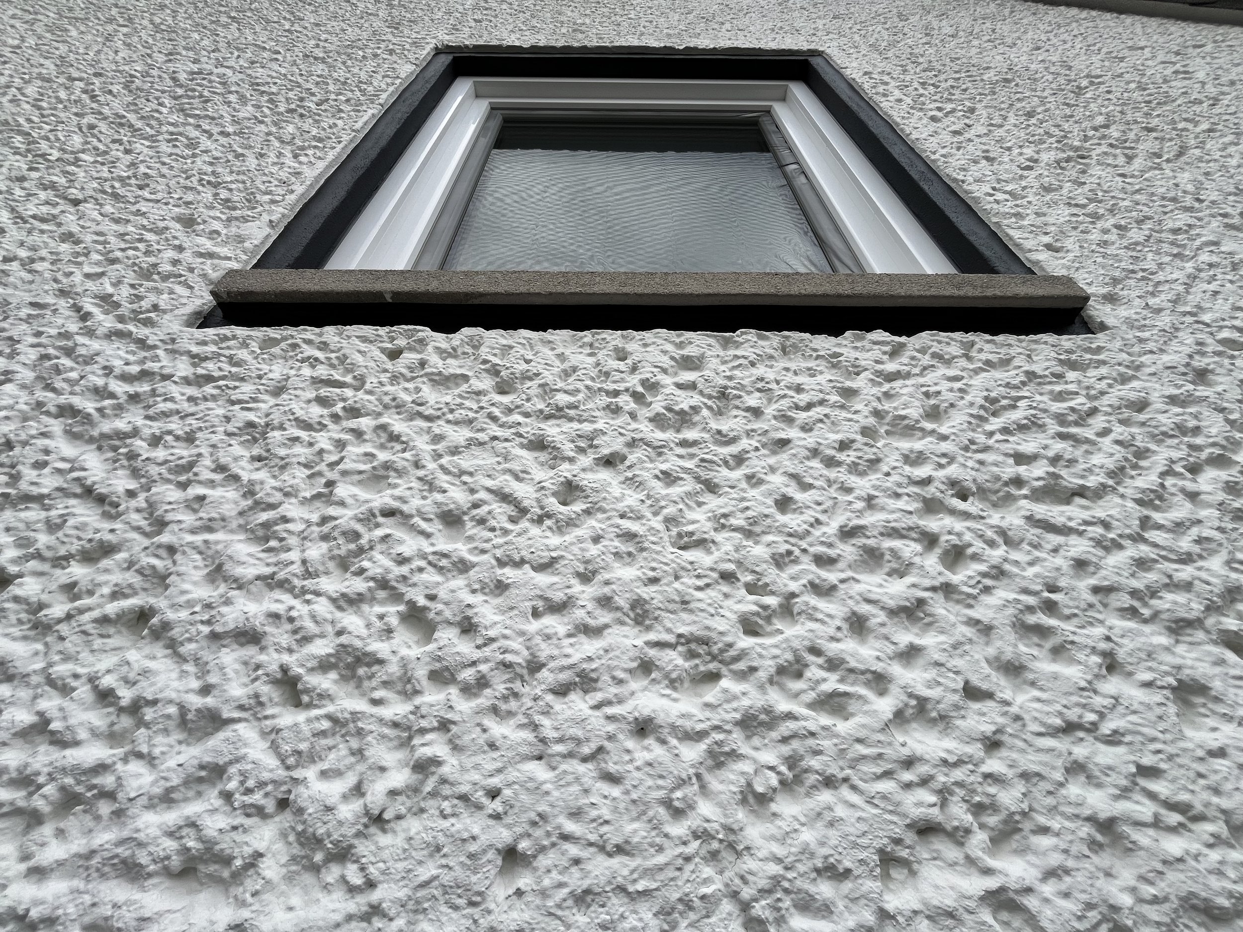 Perspektive eines Fensters mit Rahmen an einer weißen, texturierten Hauswand.