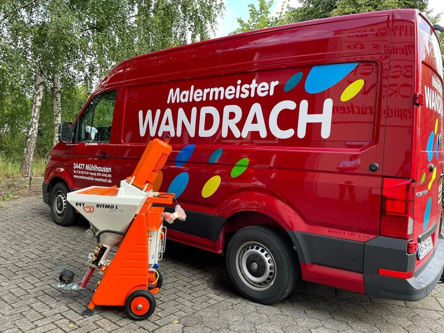 Ein roter Van mit dem Logo von Malermeister Wandrach, stehende an einer Baumreihe, davor ein industrieller Luftfilter oder Staubsauger auf einem Wagen.