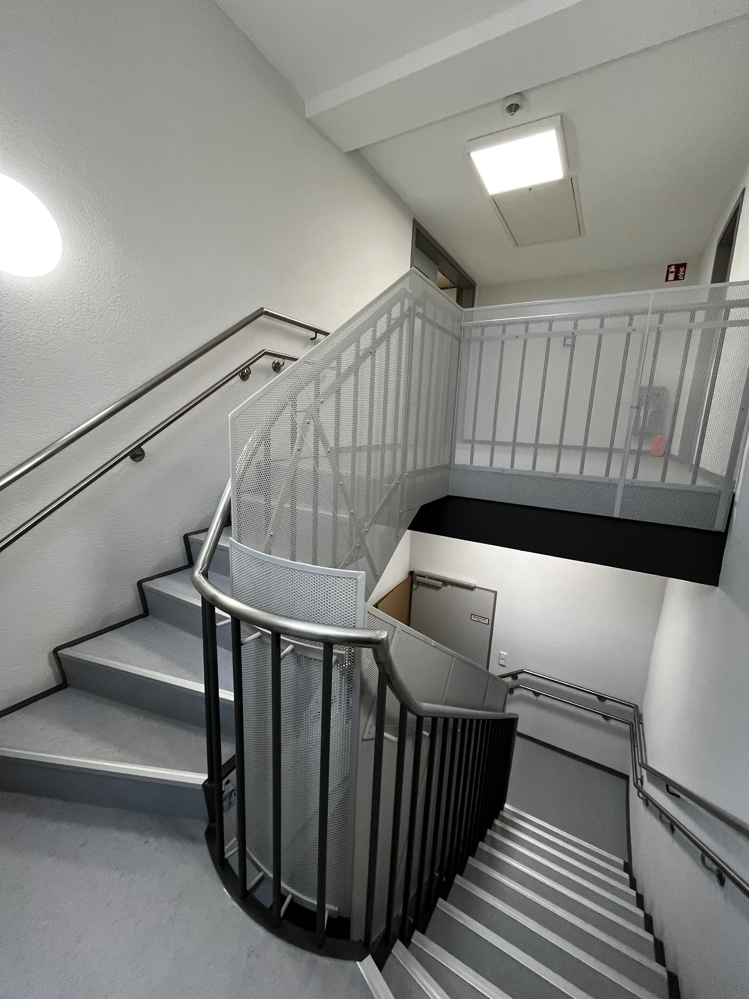 Innenaufnahme einer modernen Treppe mit Metallgeländern und weißen Wänden in einem Gebäude.