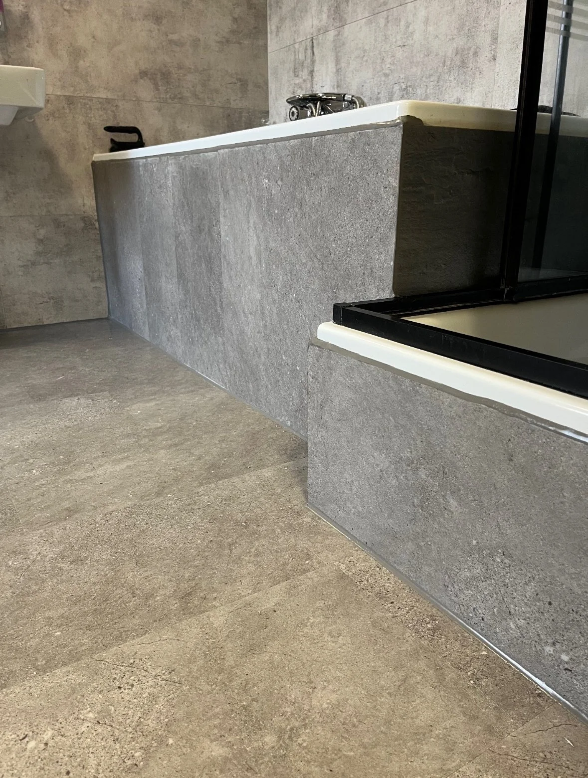 Badezimmer mit grauer Fliesenwand, Badewanne und Duschkabine.