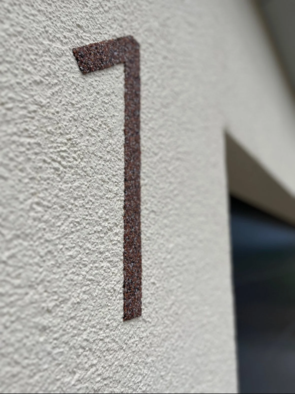 Nahaufnahme einer weißen Wand mit einer eingearbeiteten, rustfarbenen Zahl '1' aus kleinen Steinen.