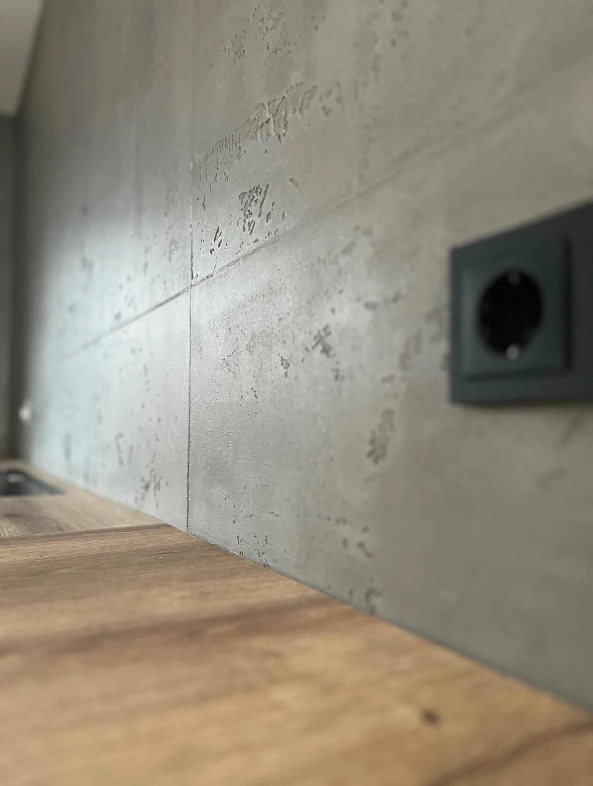 Nahaufnahme einer Wand mit Steckdose und Holzboden, Fokus auf die Wand mit sichtbaren Strukturen und Texturen.