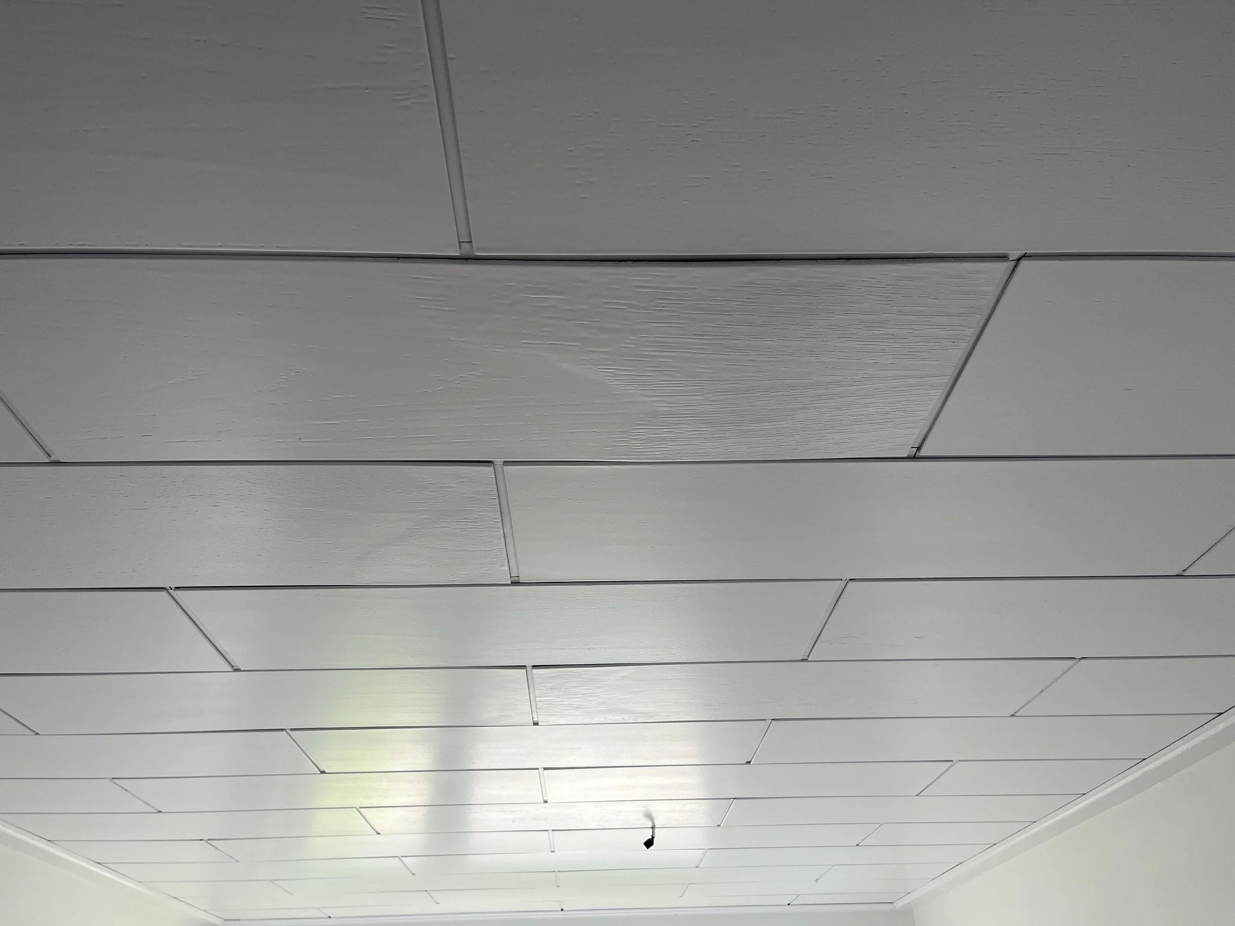 Decke mit weißen Paneelen und einer aufgehängten Lampe in einem Raum.