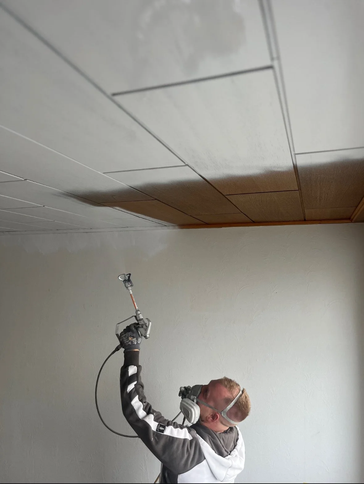 Ein Mann trägt Schutzbrille und Gehörschutz, während er mit einem Drucksprühgerät eine Wand streicht.